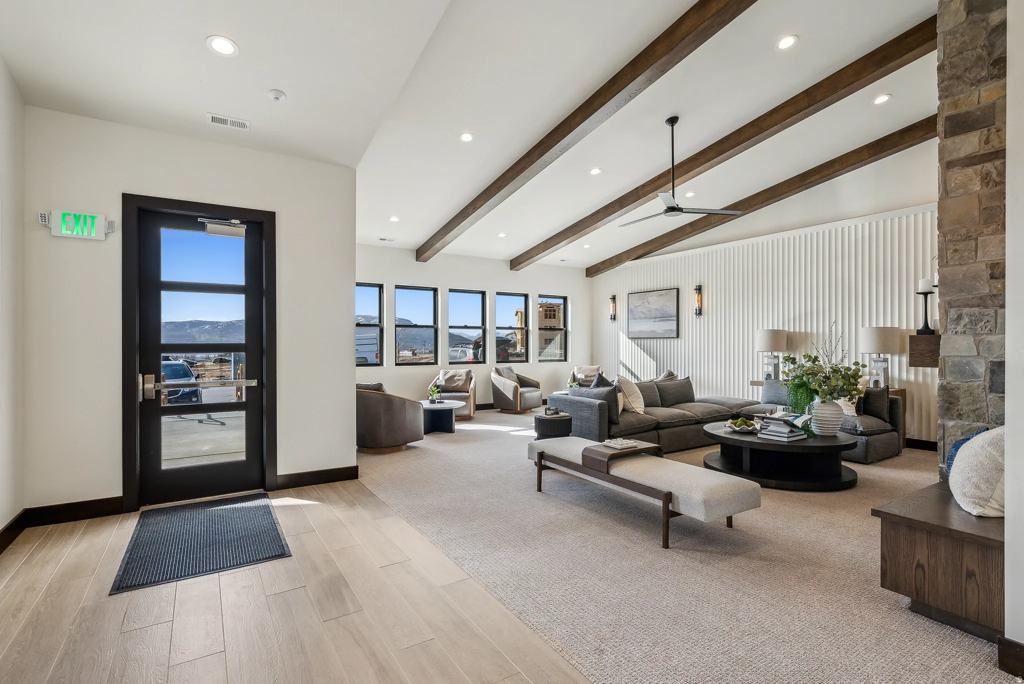 Spacious living area featuring wood-finish flooring, a vaulted ceiling with exposed beams, recessed lighting, and a stone-clad fireplace