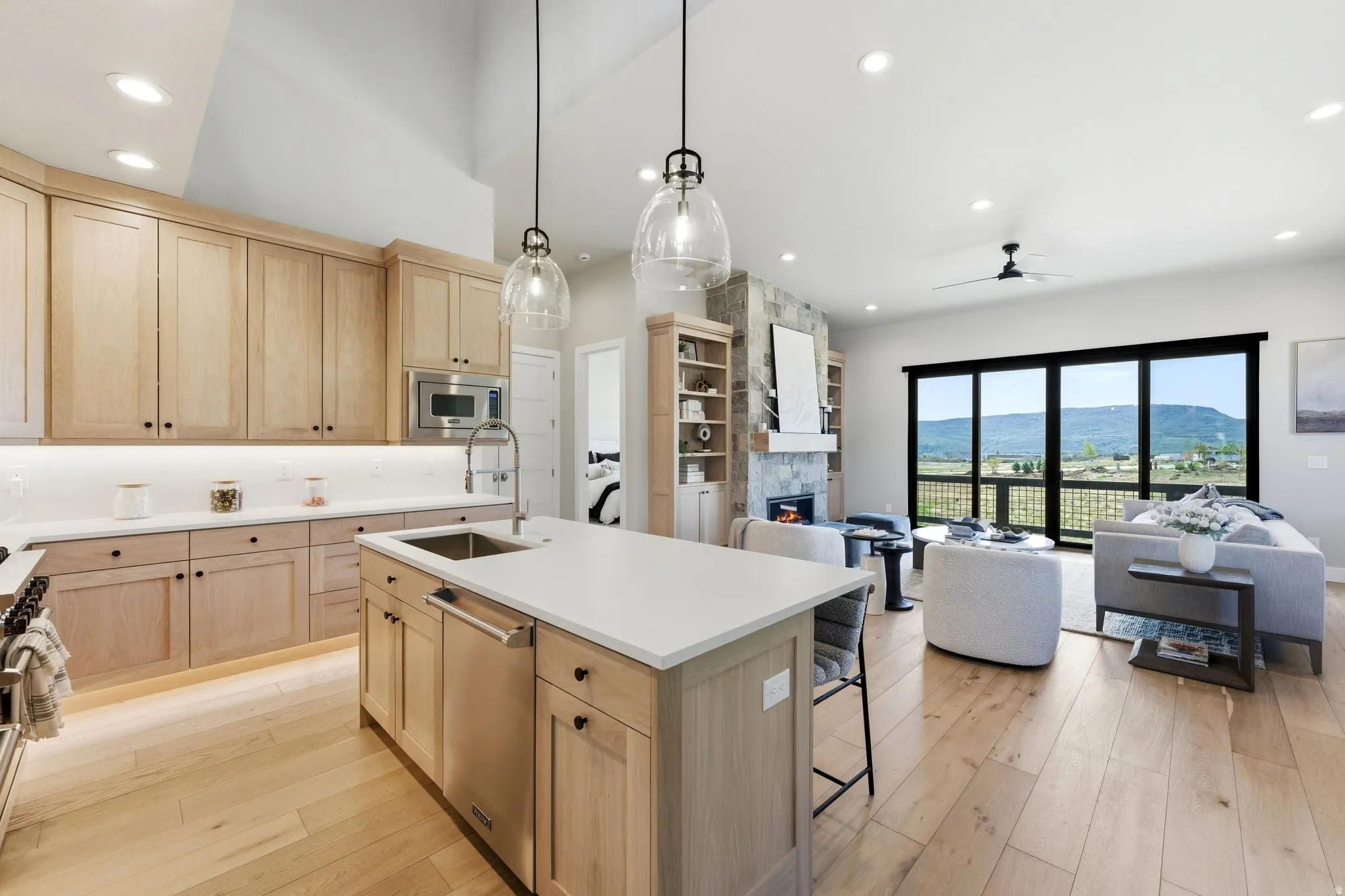 Open concept living space featuring light wood-finish flooring, a kitchen island with integrated sink, stainless steel appliances, and light wood cabinetry
