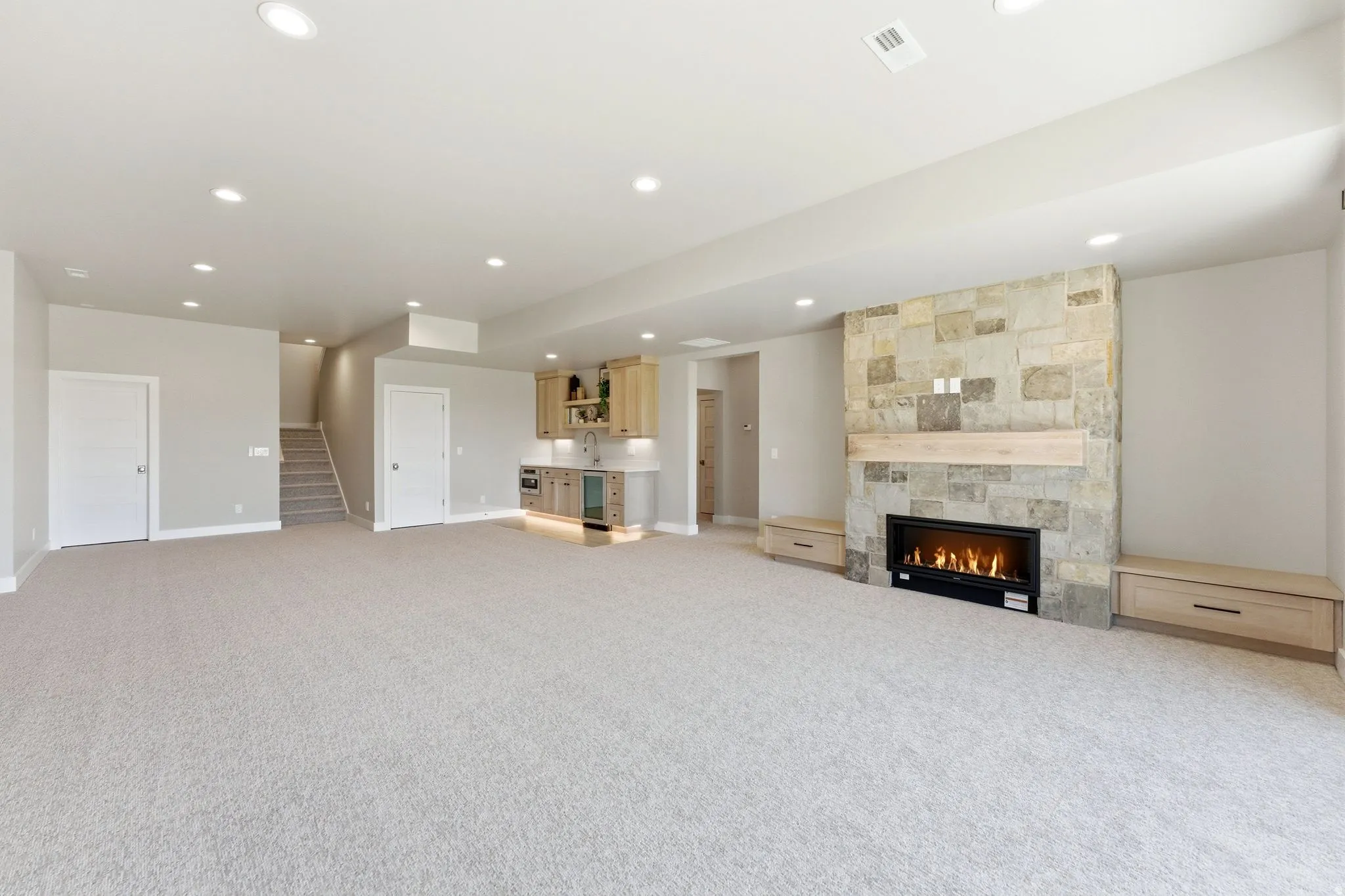 Spacious finished basement featuring a stone-clad fireplace with a natural wood mantel, built-in cabinetry, an integrated wet bar with a wine cooler, and recessed lighting