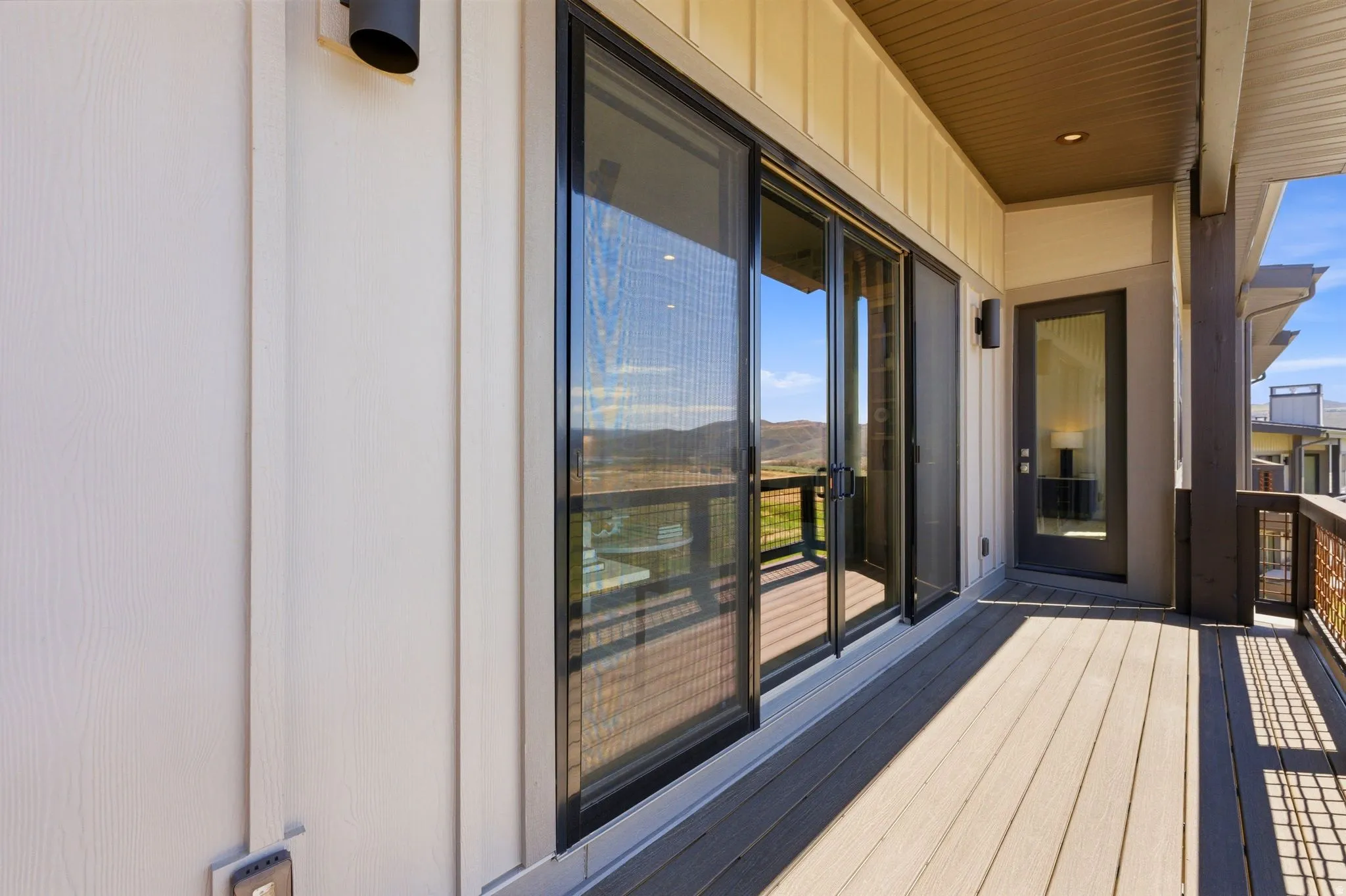 Expansive outdoor deck featuring wood-finish flooring, a sliding glass door system, and a black framed entry door