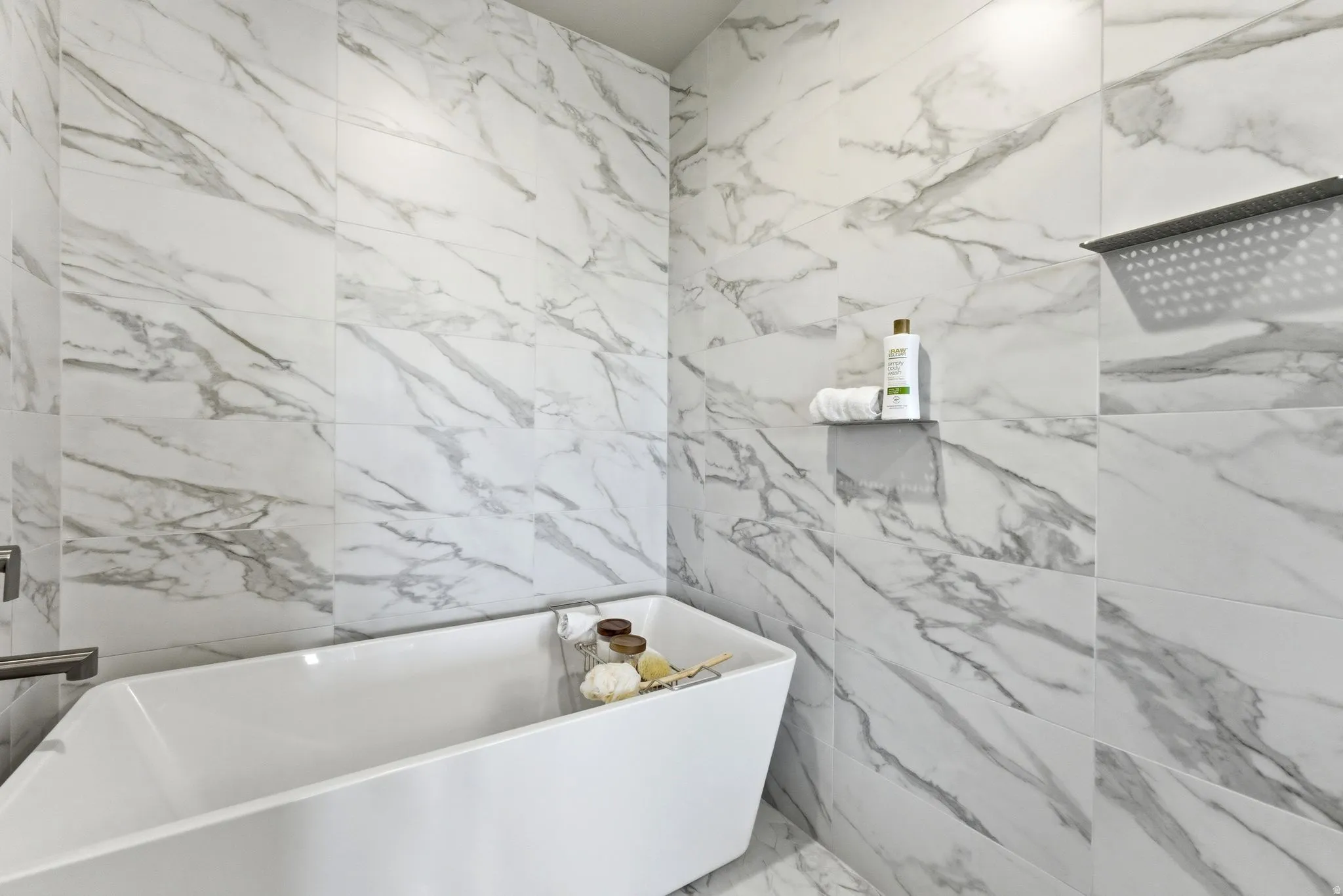 Bathroom featuring a freestanding soaking tub, marble-look wall tile, and a rain shower fixture