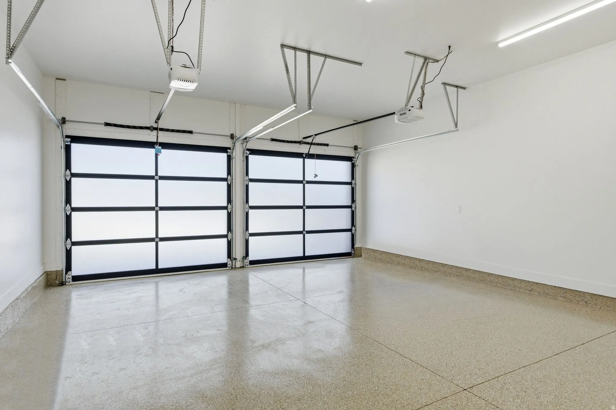 Spacious garage featuring two modern glass panel doors, a durable speckled epoxy floor, bright overhead strip lighting, and automatic garage door openers