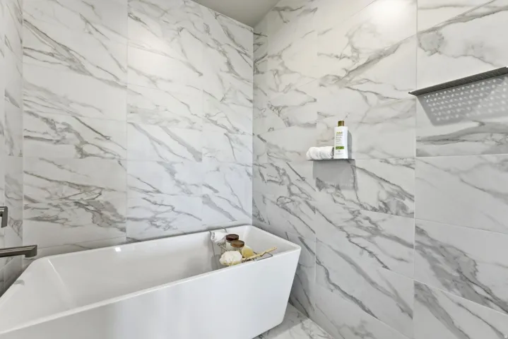 Bathroom featuring a freestanding soaking tub, marble-look wall tile, and a rain shower fixture