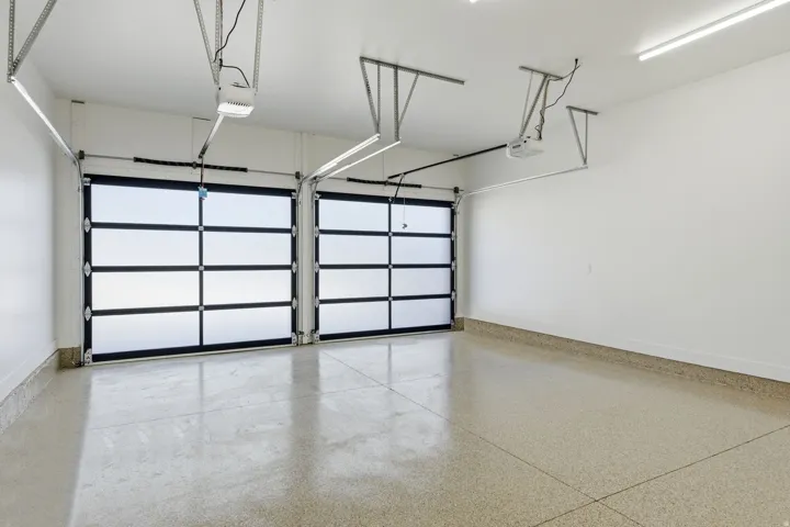 Spacious garage featuring two modern glass panel doors, a durable speckled epoxy floor, bright overhead strip lighting, and automatic garage door openers