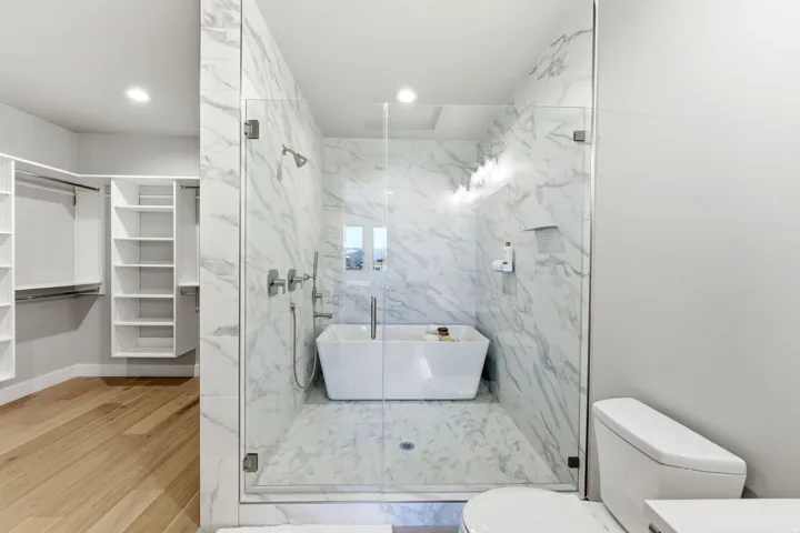 Glass-enclosed wet room featuring a freestanding soaking tub and full-height marble-style tile