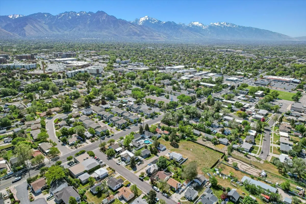 Expansive aerial perspective showcasing a residential neighborhood with tree-lined streets, surrounded by commercial and multi-unit properties