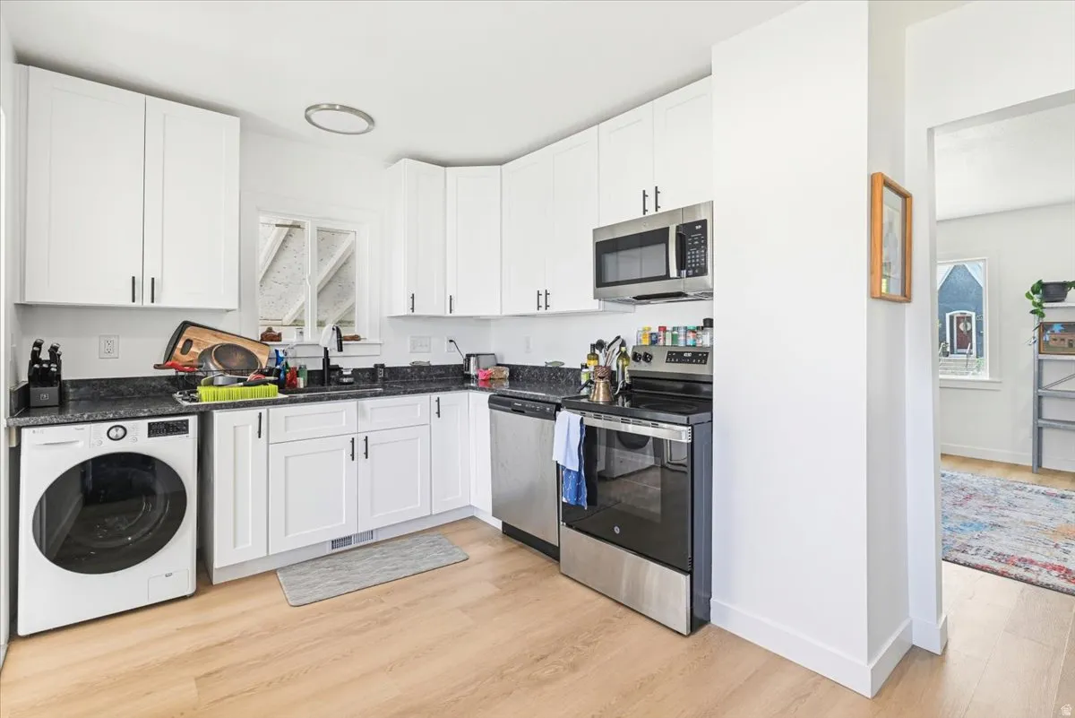 Kitchen featuring white cabinetry with dark hardware, dark countertops, stainless steel appliances, and wood-finish flooring