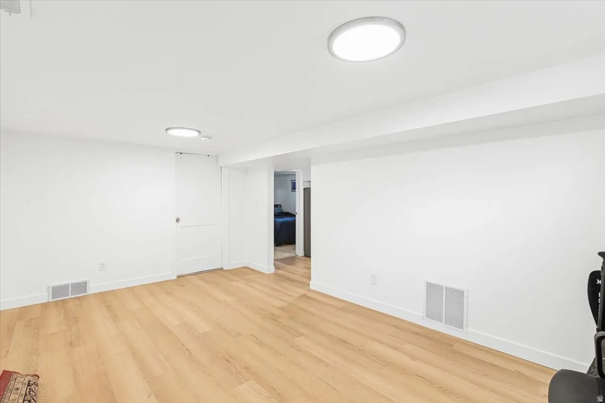Spacious room featuring light wood-finish flooring, white walls, and recessed lighting fixtures