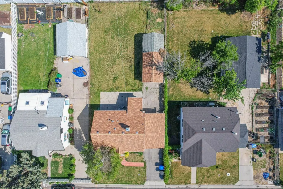 Aerial view of a residential property featuring a brown shingle roof, a detached garage, an extensive concrete driveway, and a large grassy yard