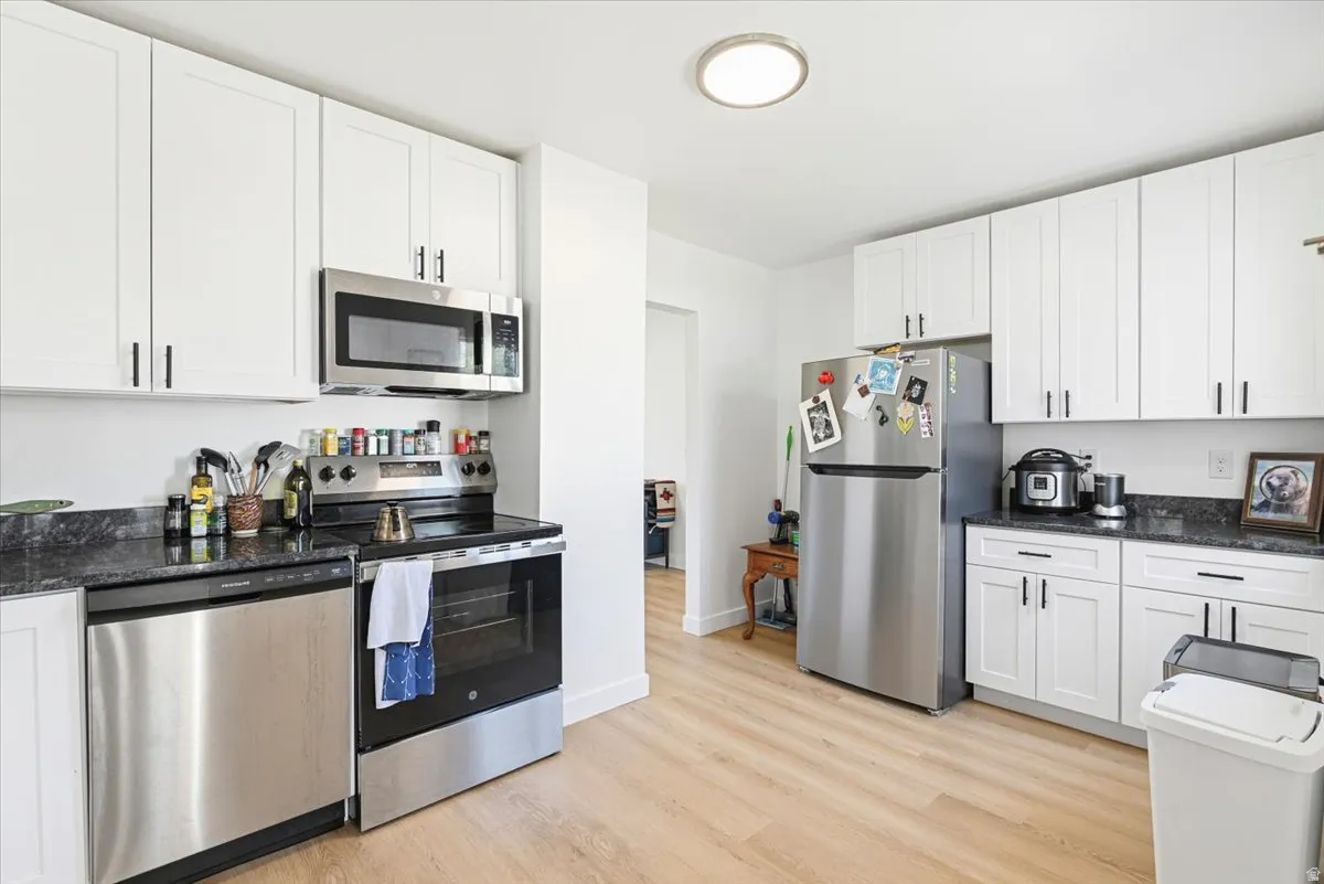 Kitchen featuring light wood-finish flooring, white cabinetry with black hardware, dark countertops, and stainless steel appliances