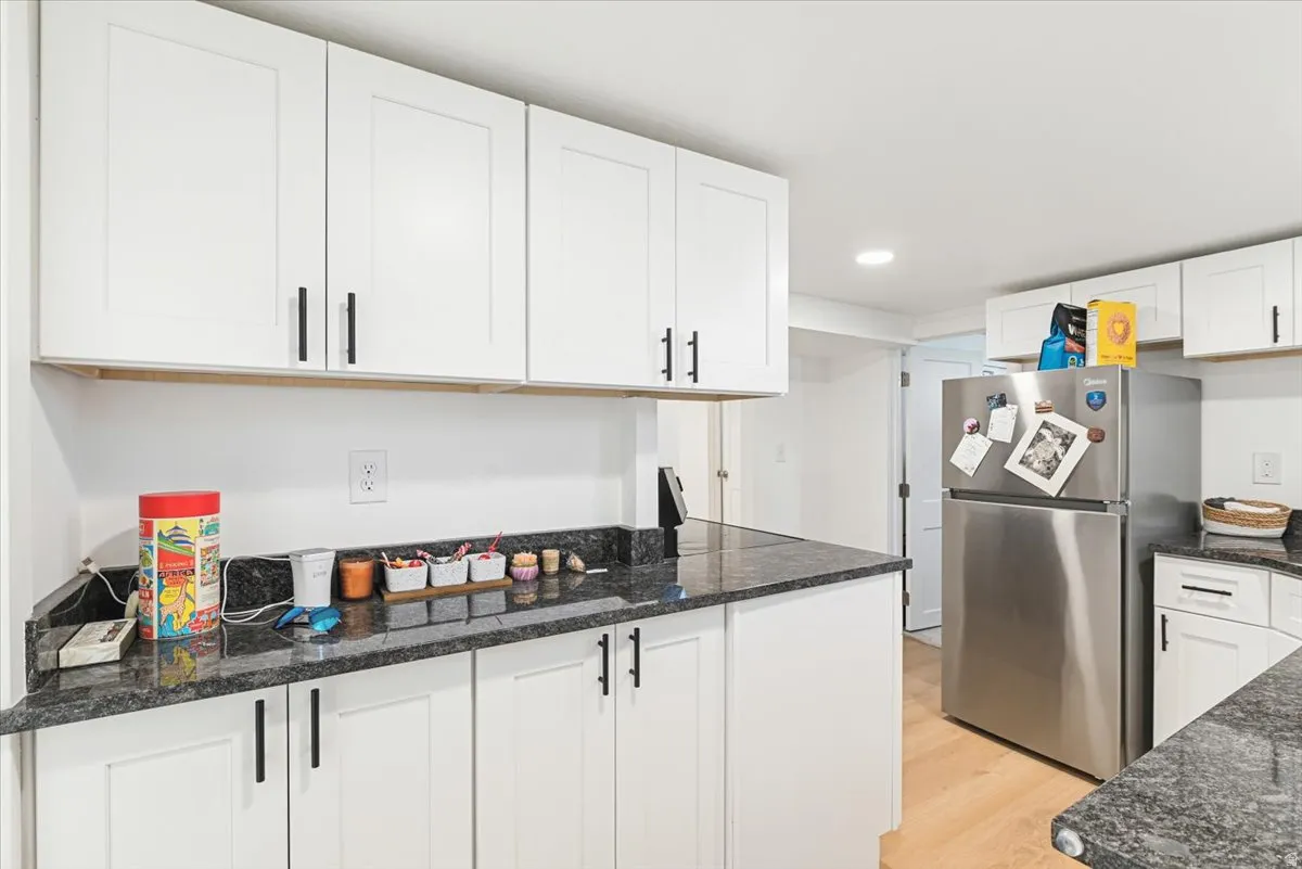 Kitchen featuring white shaker-style cabinetry, black hardware, dark stone countertops, and wood-finish flooring