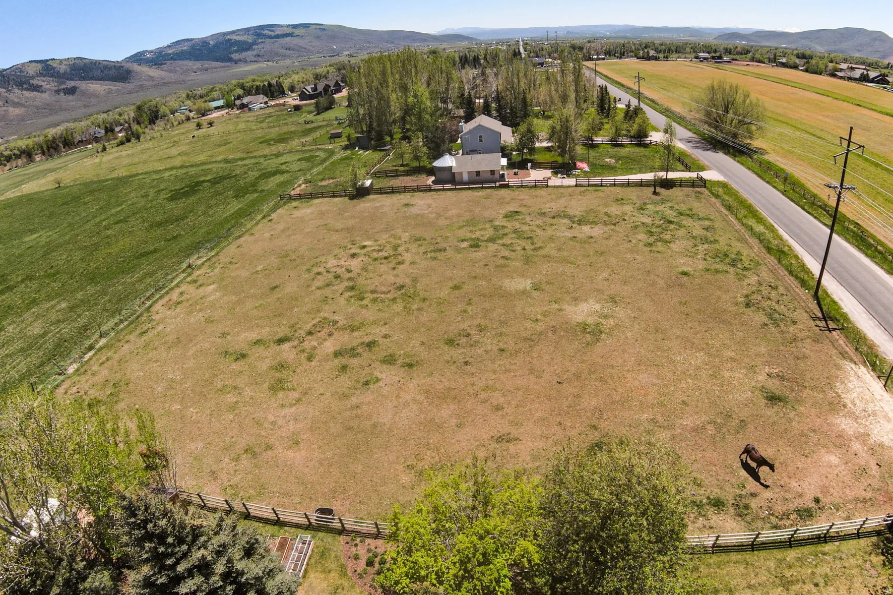 Expansive, fenced pasture land with a distant light-colored dwelling, adjacent to a paved road