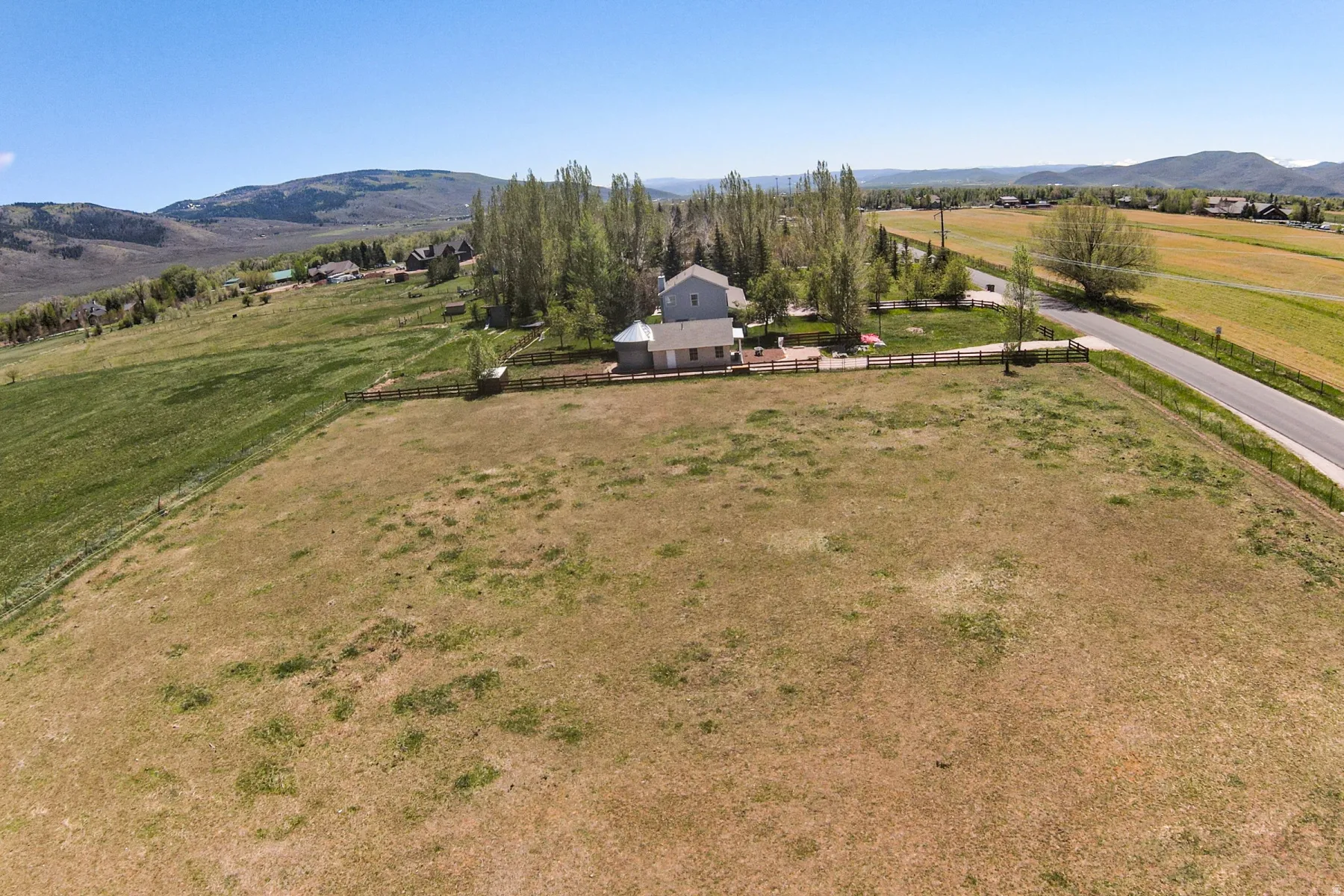 Expansive open land featuring a split-rail fence, mature trees, and mountainous terrain in the distance