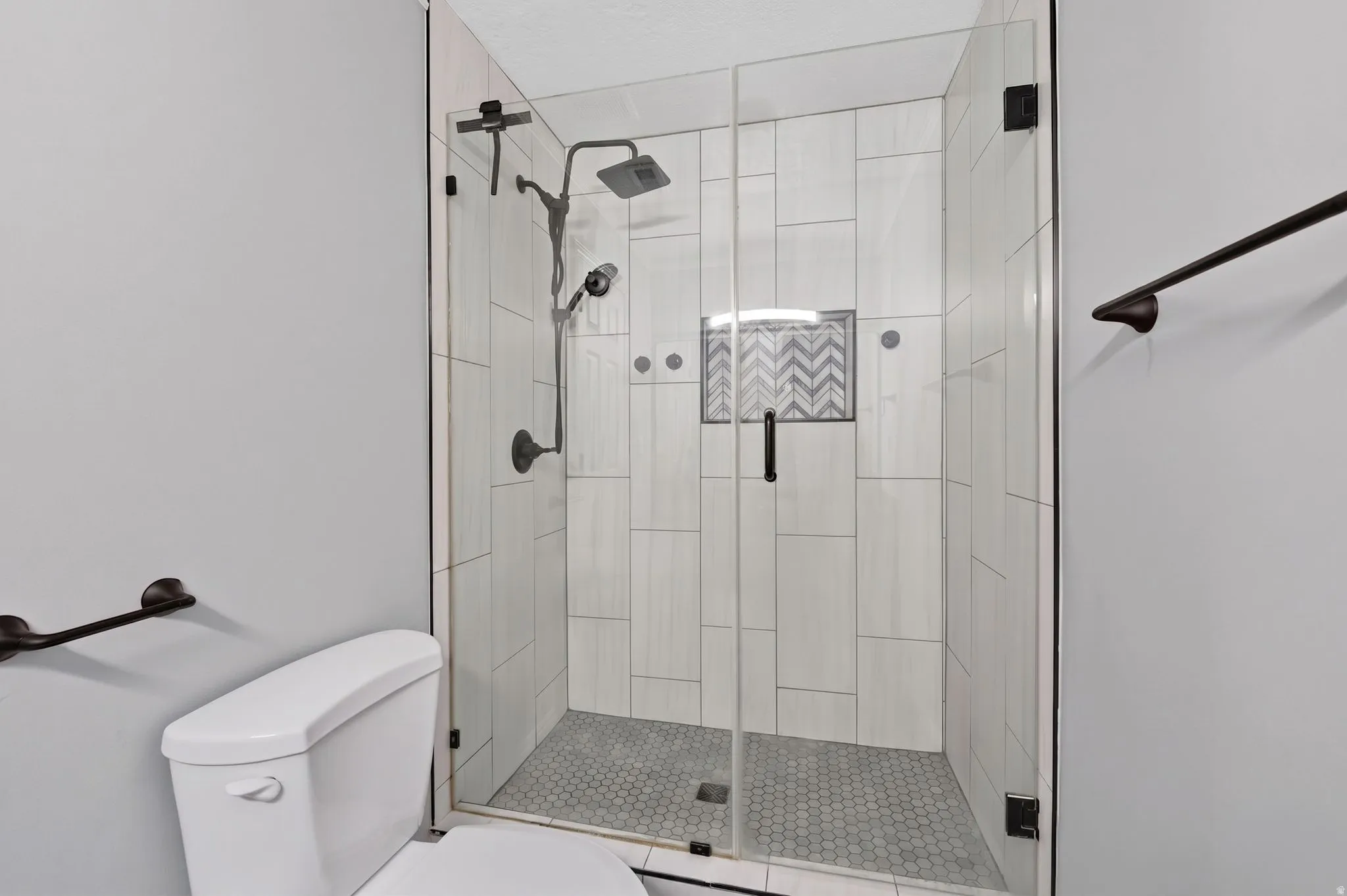 Glass-enclosed shower featuring a rainfall showerhead, handheld sprayer, and dark bronze fixtures