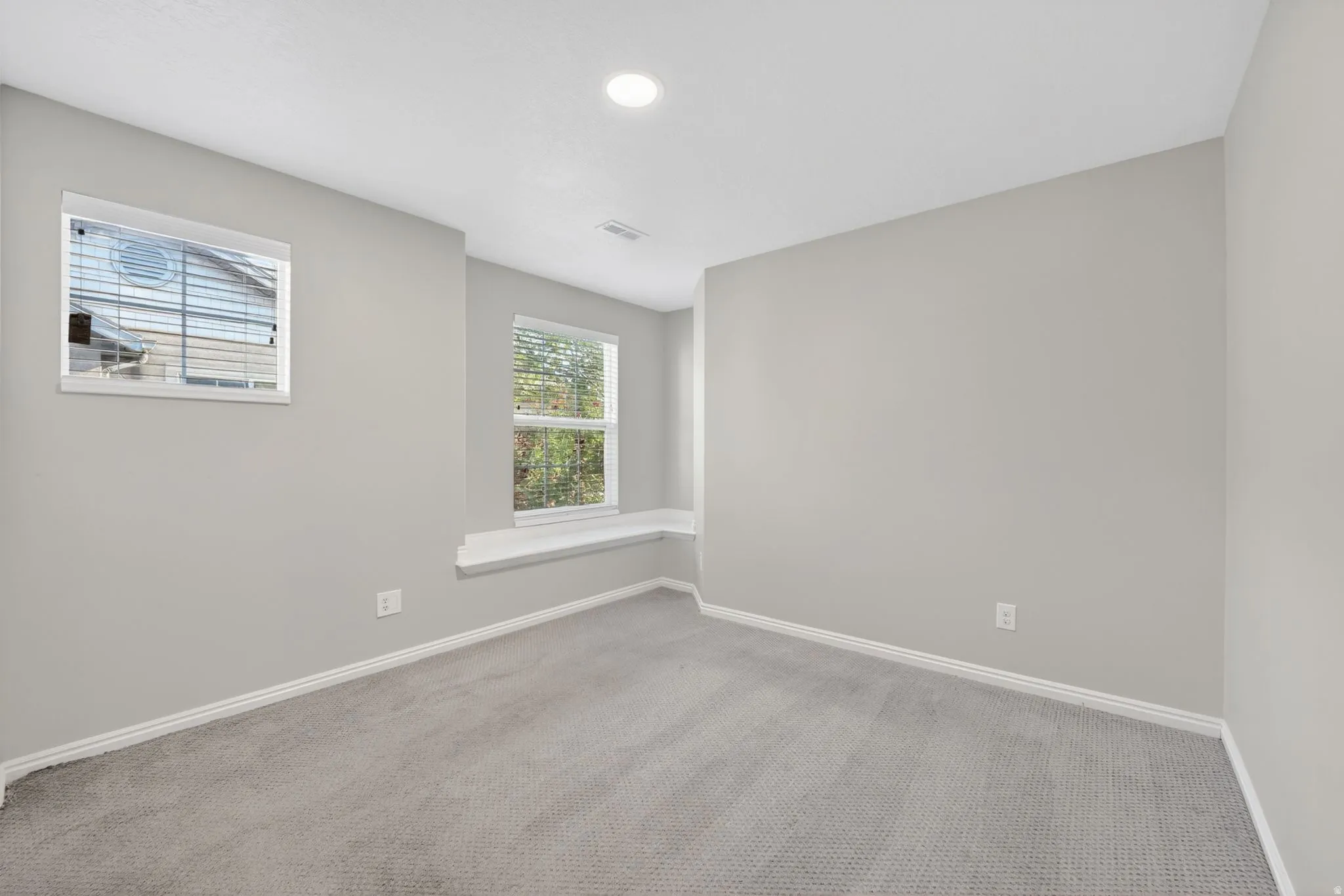 Carpeted room featuring light gray walls, two windows, and a built-in window bench