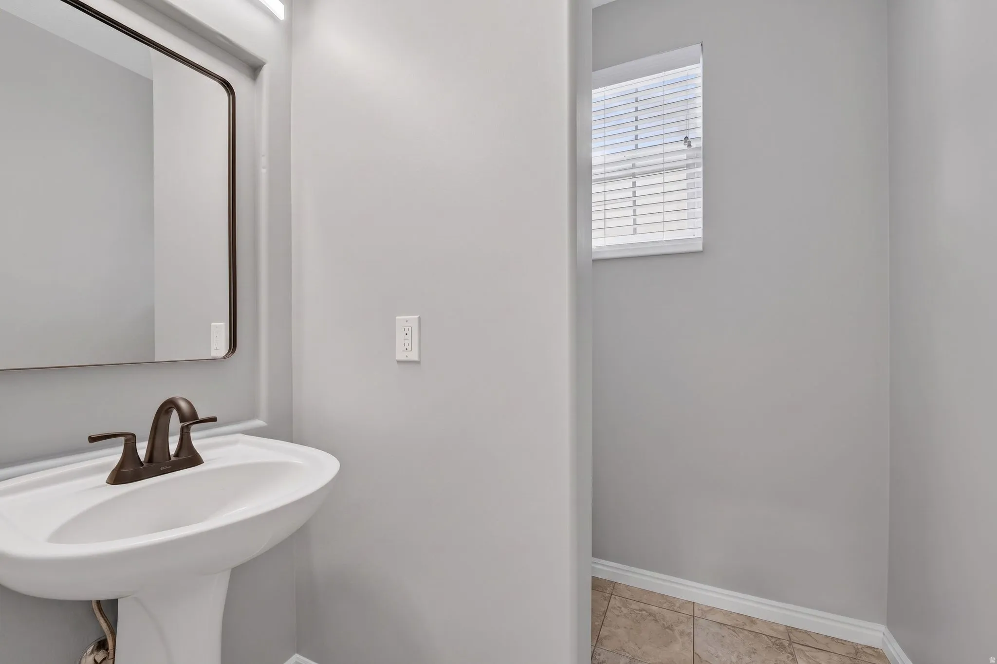 Pedestal sink with bronze-finish faucet, rectangular mirror, and overhead lighting