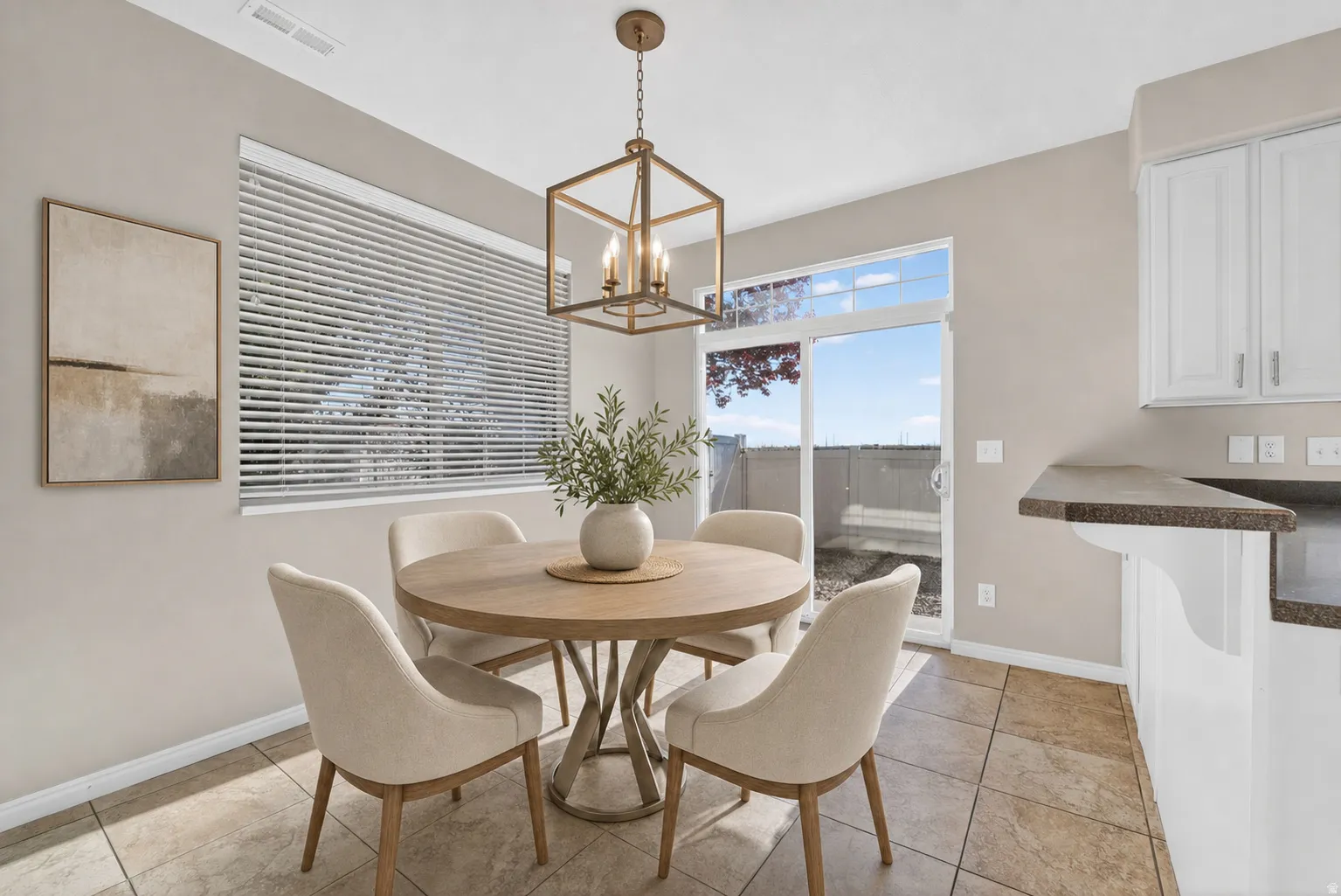 Dining area featuring tile flooring, a large window with blinds, a sliding glass door for outdoor access, a geometric pendant light fixture, and an adjacent counter space with white cabinetry