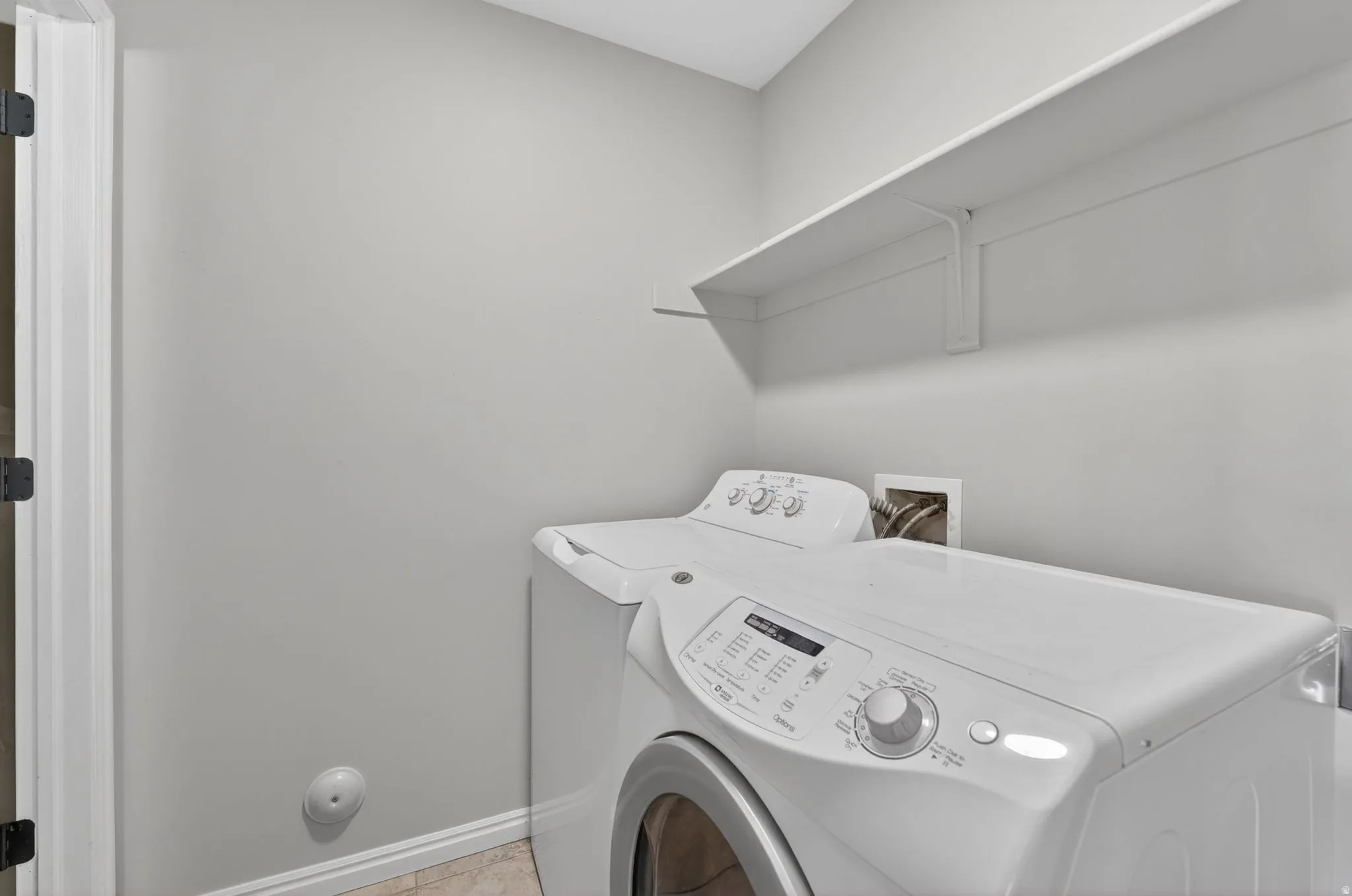 Dedicated laundry area featuring a white wall shelf, light gray wall paint, and white baseboards