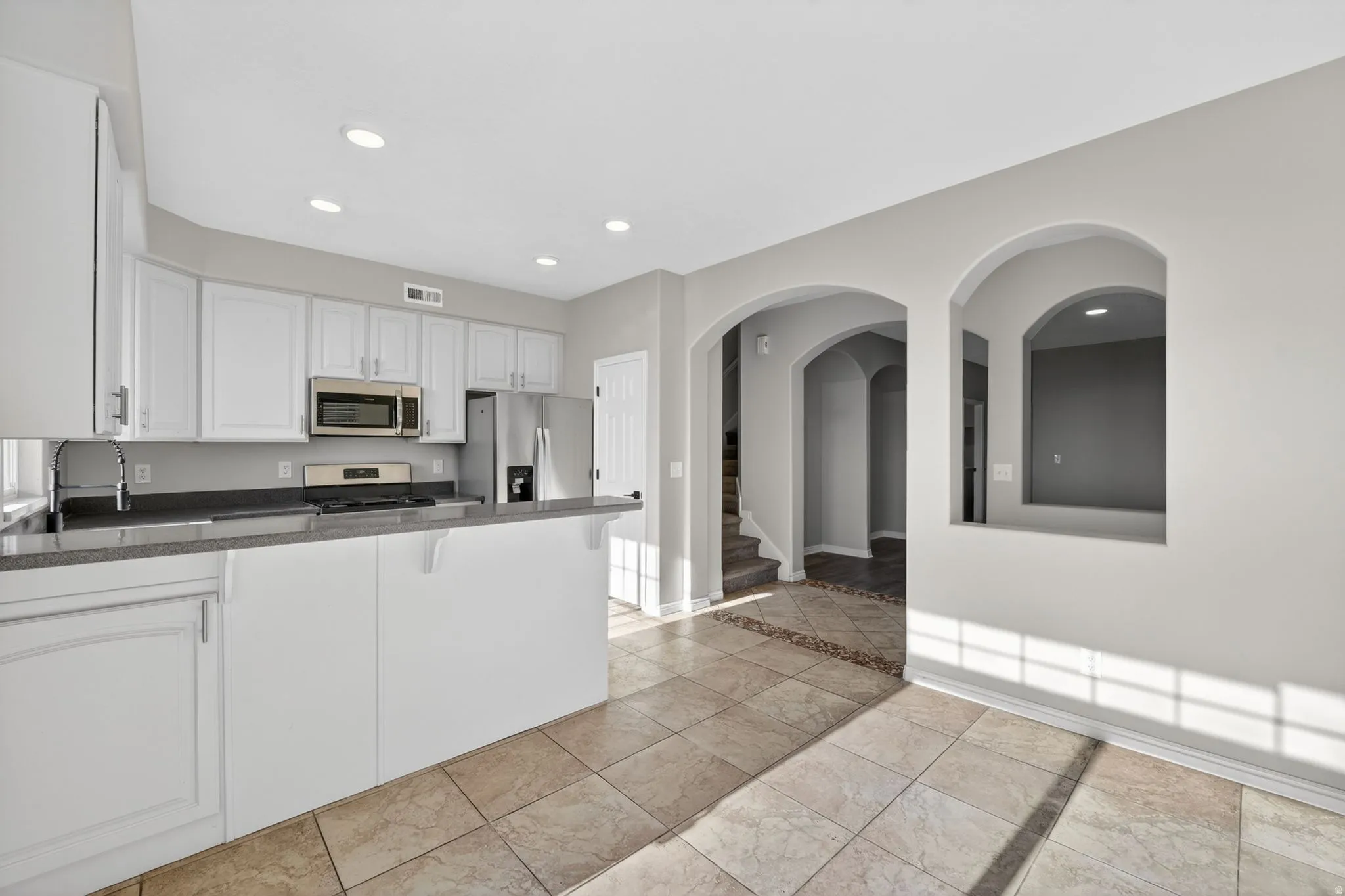 Open-concept kitchen with recessed lighting, white cabinetry, dark countertops, and stainless steel appliances
