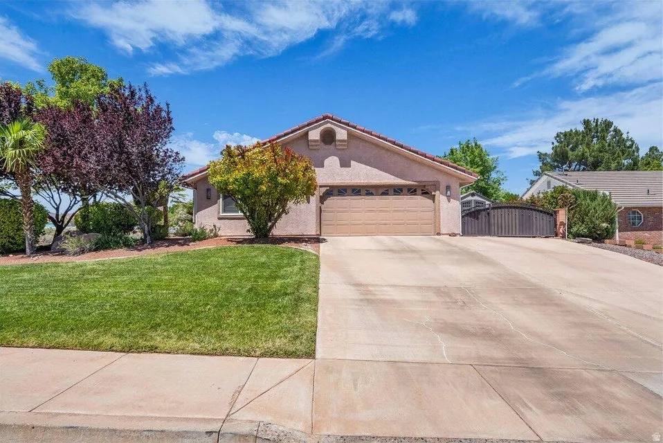 Stucco exterior residence featuring a terracotta-style tile roof, an integrated two-car garage, a concrete driveway, and a manicured lawn with mature landscaping