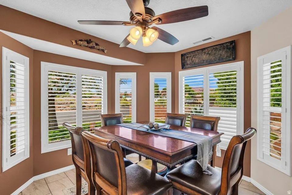 Bay window with white plantation shutters, an overhead ceiling fan with integrated lighting, and tile flooring