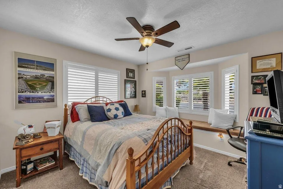 Bedroom featuring a wood-finish ceiling fan with integrated lighting, a bay window with a built-in window seat, and white plantation shutters