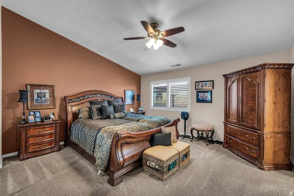Bedroom featuring an accent wall, sloped ceiling, ceiling fan, carpet flooring, and a window with plantation shutters