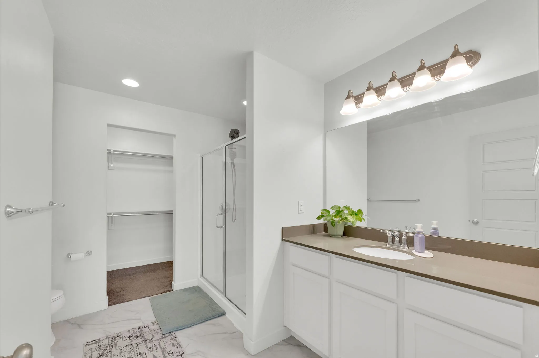 Bathroom featuring a single vanity with an integrated sink, broad mirror, and a five-light fixture
