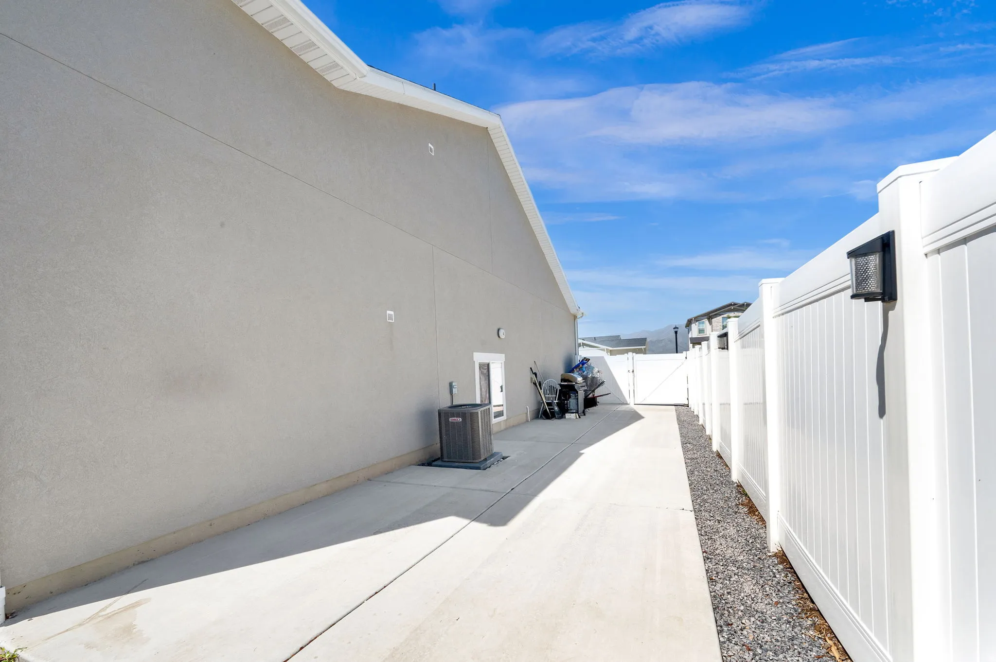 Concrete RV parking alongside of home, featuring a white vinyl fence and a gravel strip