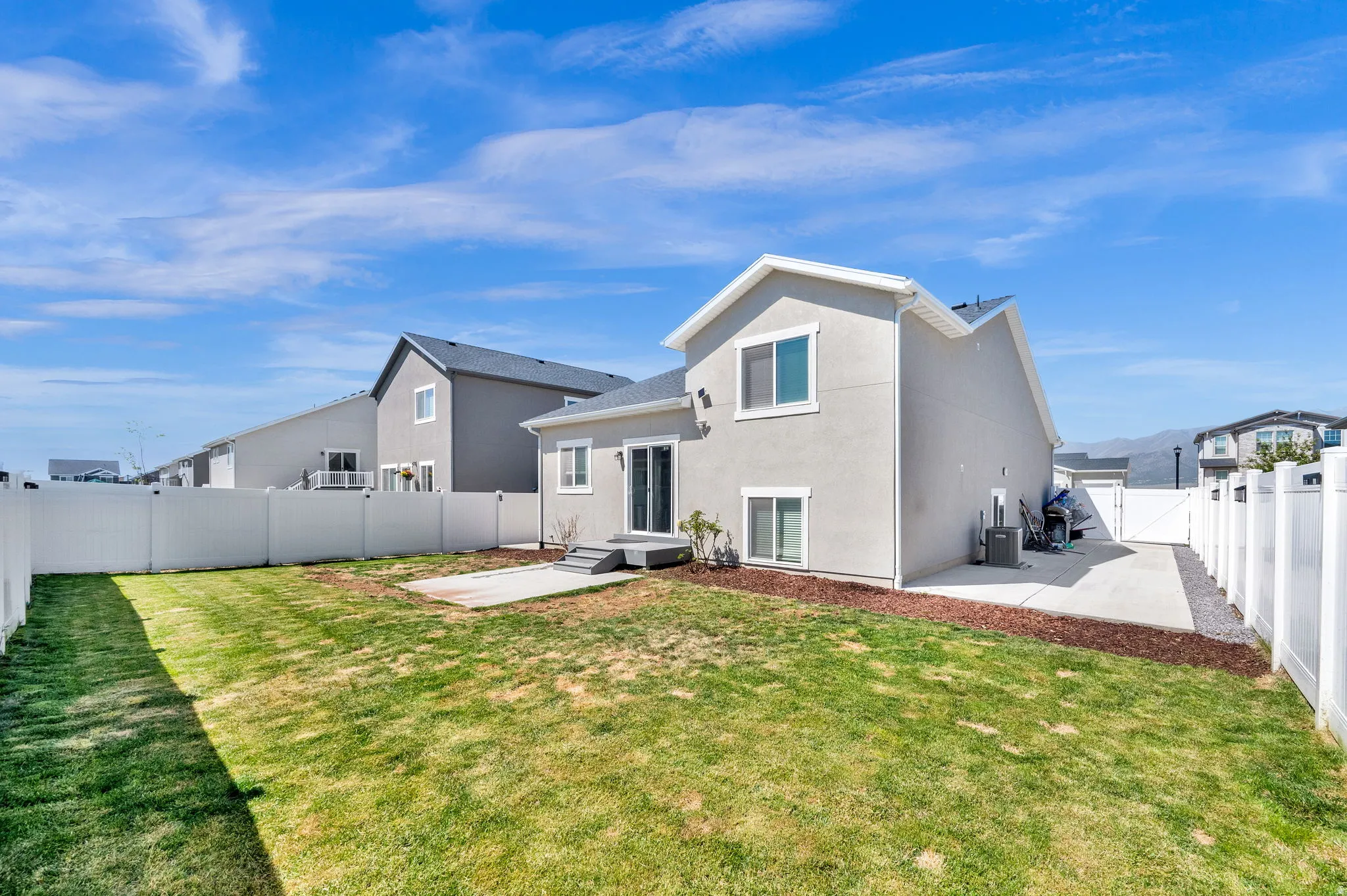 Rear exterior featuring a spacious lawn, white privacy fencing, and a concrete patio