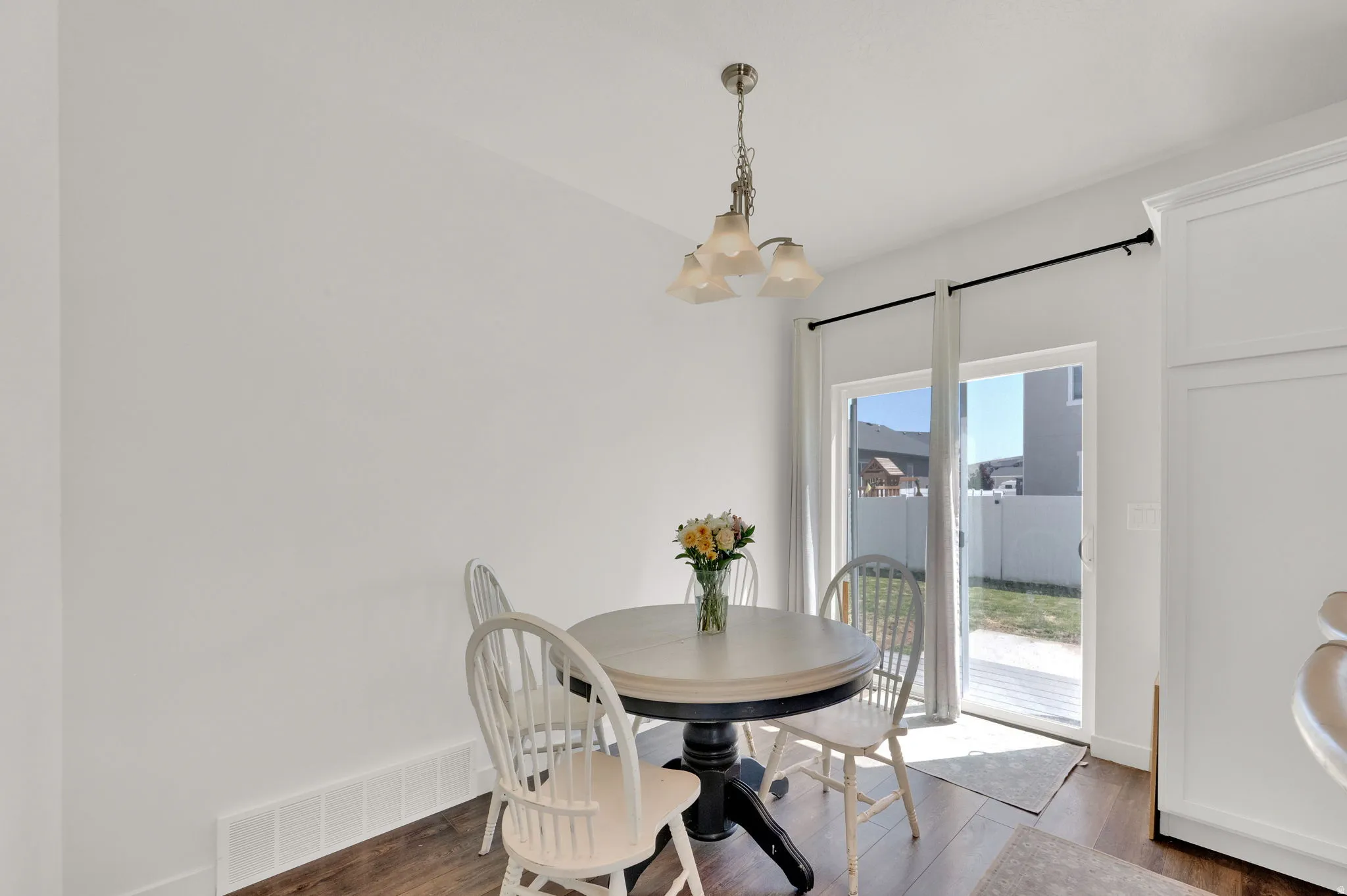 Dining area with wood-finish flooring, a contemporary chandelier, and direct patio access through a double-pane sliding glass door