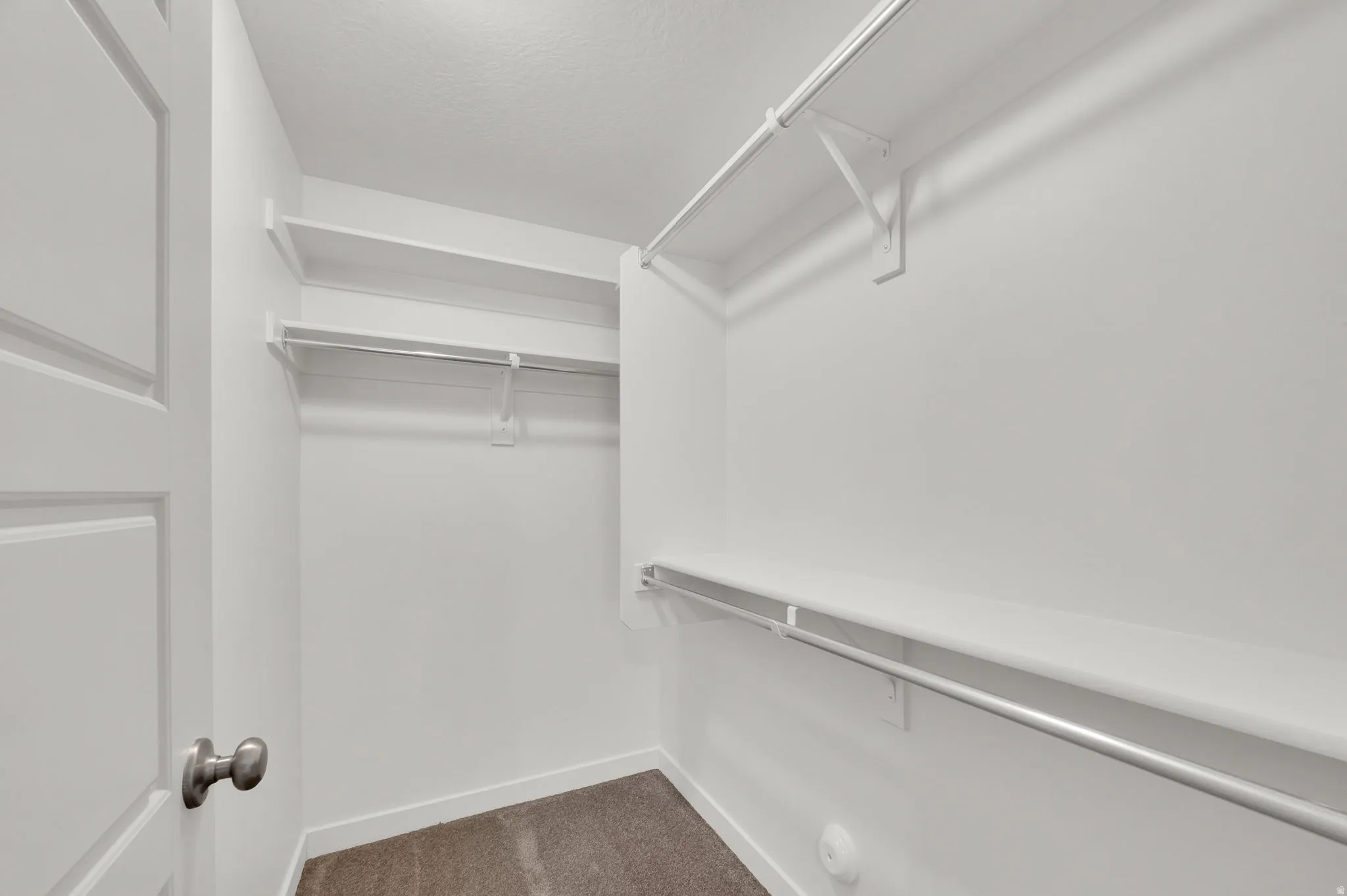 Walk-in closet featuring white walls, white shelving, and chrome hanging rods