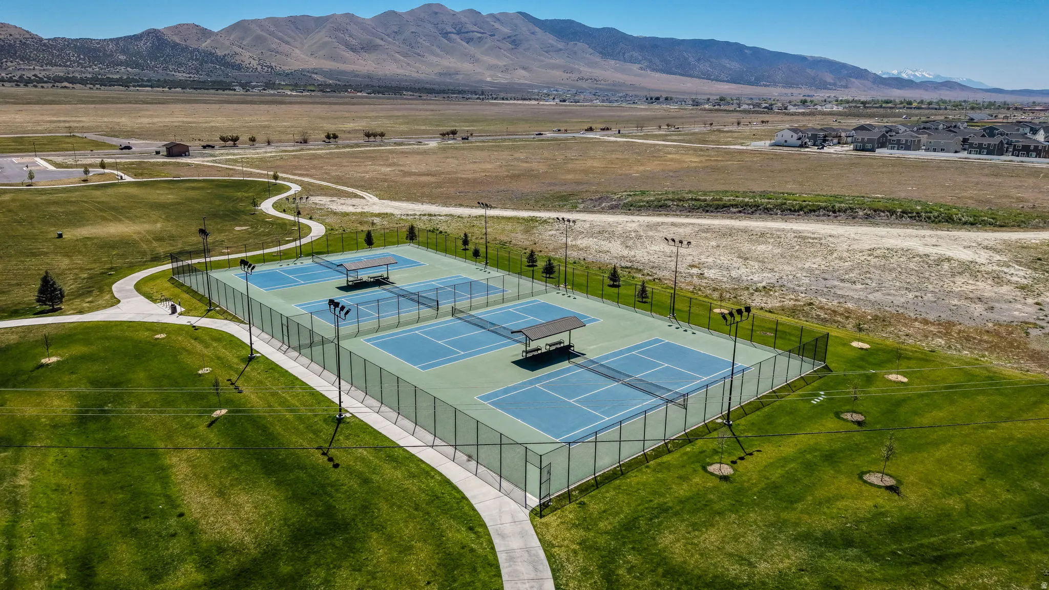 Community amenity featuring multiple tennis courts with light standards, perimeter fencing, and shade structures