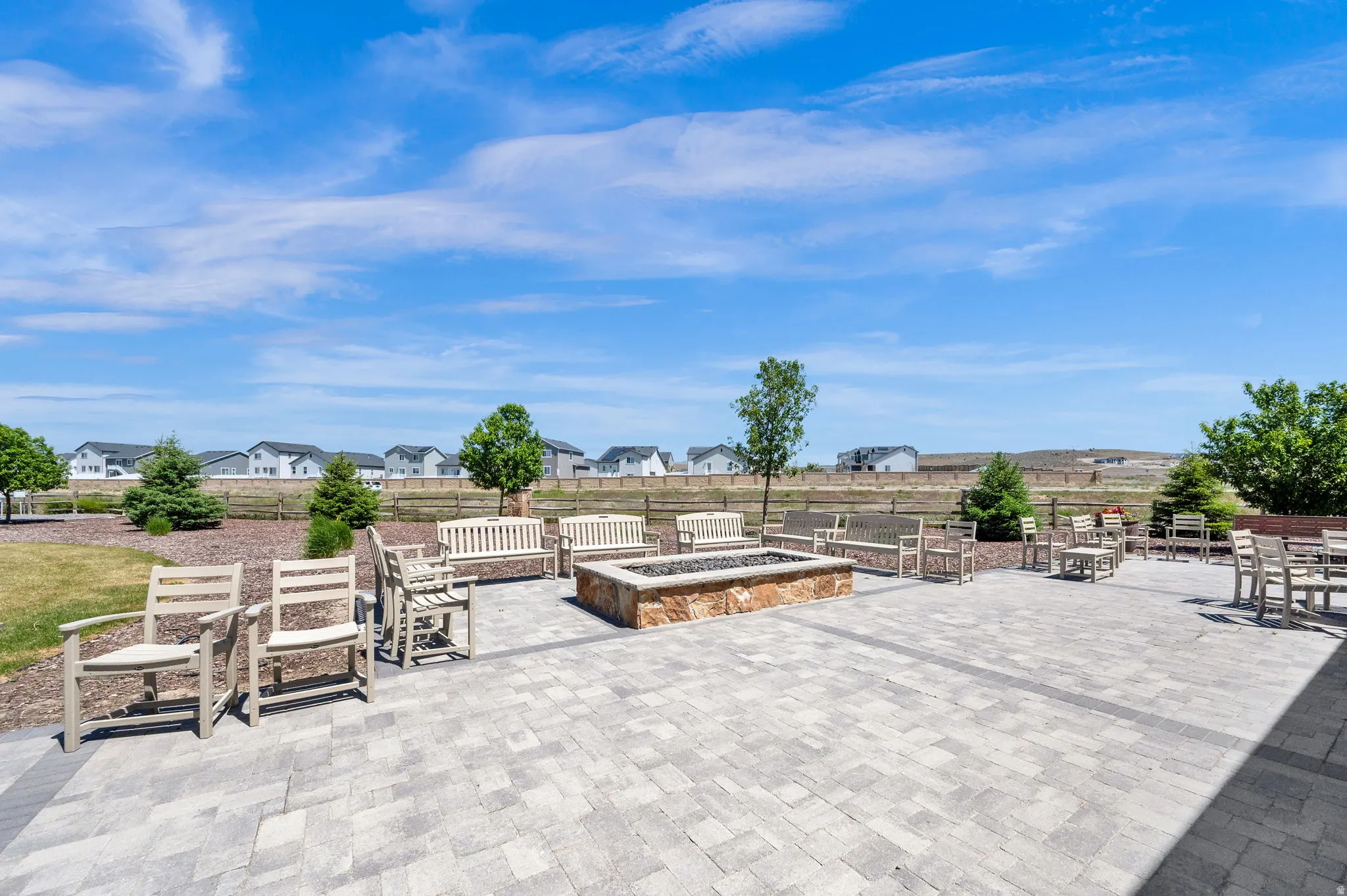 Expansive paver patio featuring a stone-clad fire pit, multiple seating areas with benches and chairs, and surrounding landscaping