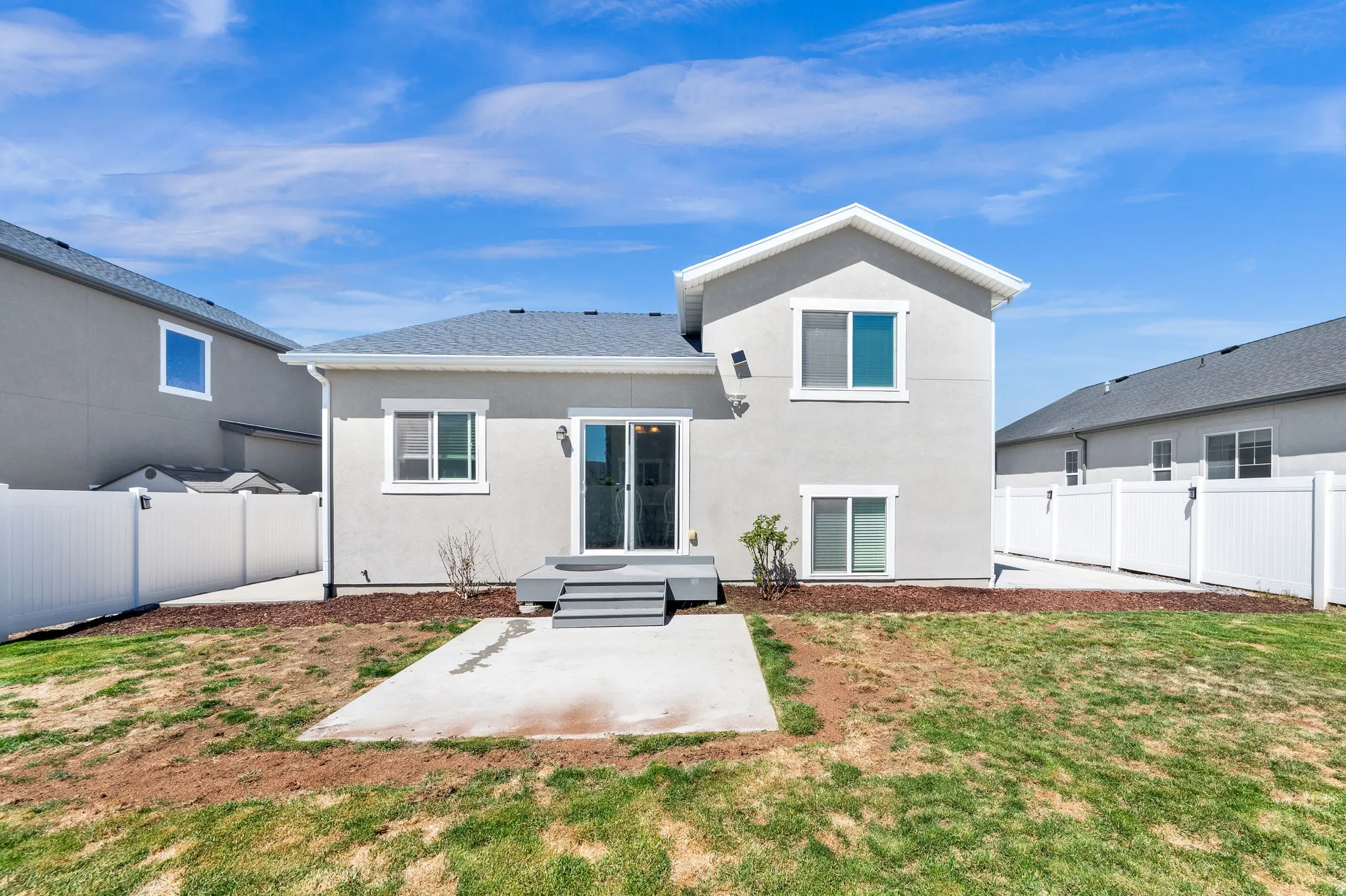 Rear exterior featuring a sliding glass door, multiple windows, a small raised deck, and a concrete patio