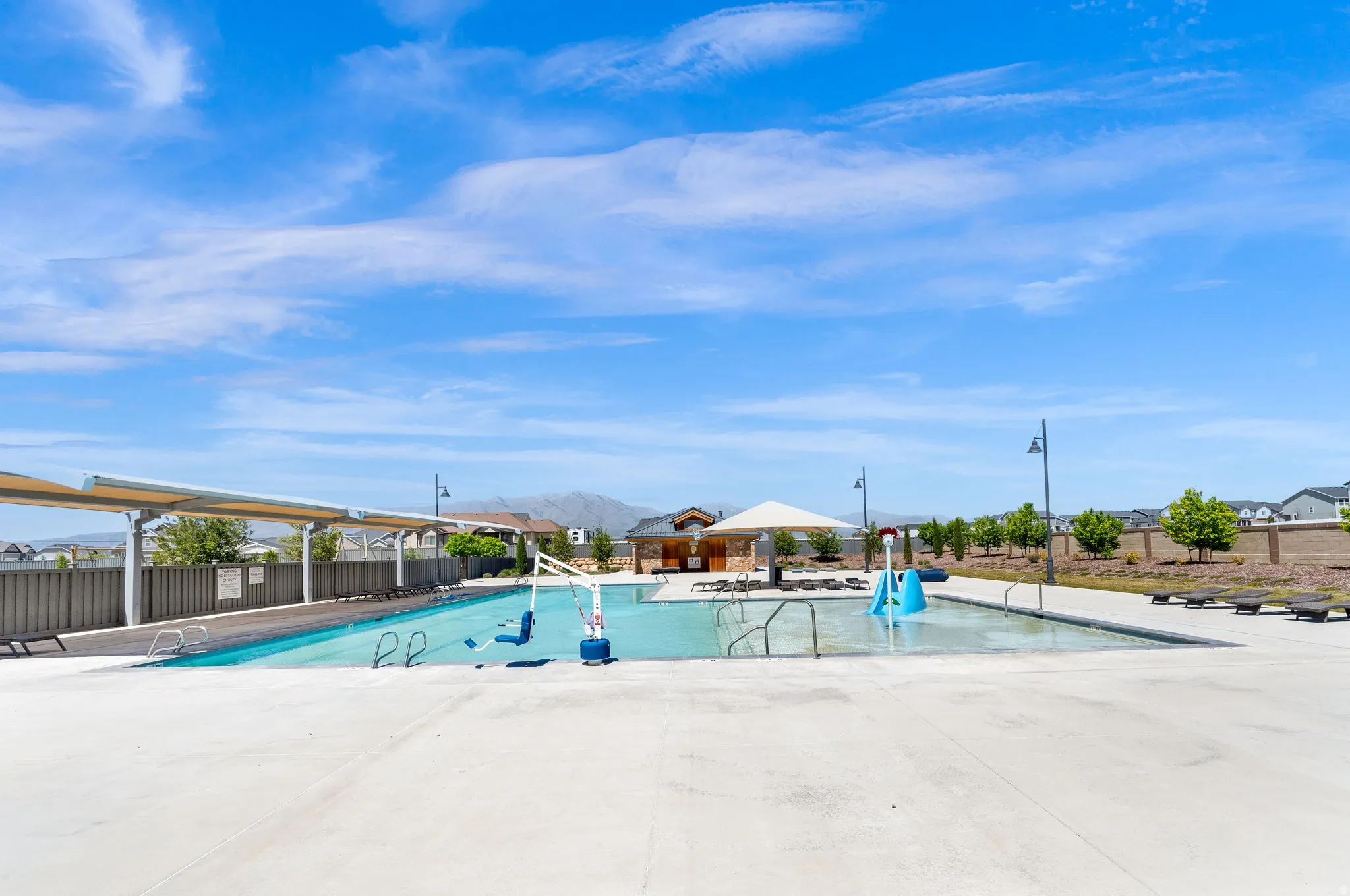 Community swimming pool featuring a shallow entry, integrated water play equipment, and shaded lounge areas
