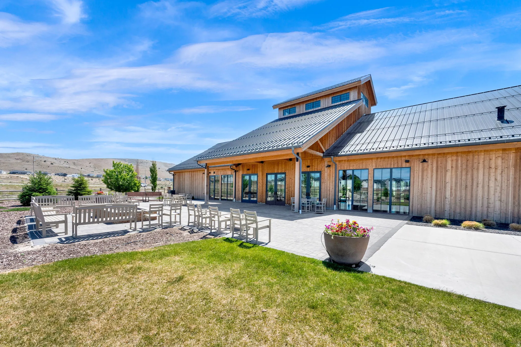 Expansive outdoor patio with multiple seating areas, a manicured lawn, and a modern wooden building with a metal roof