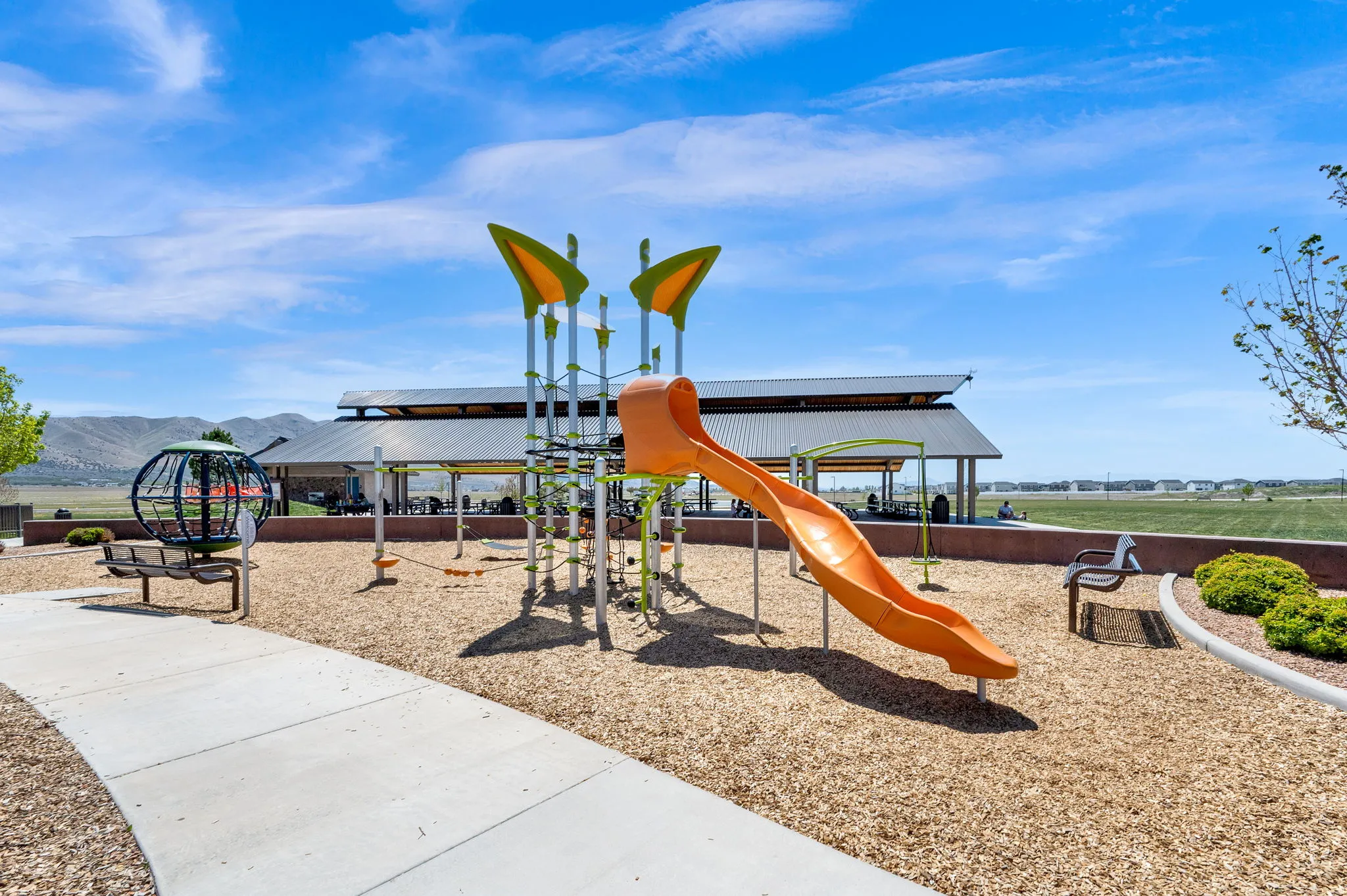 Community playground featuring a slide, climbing structures, wood chip surfacing, and a covered picnic area