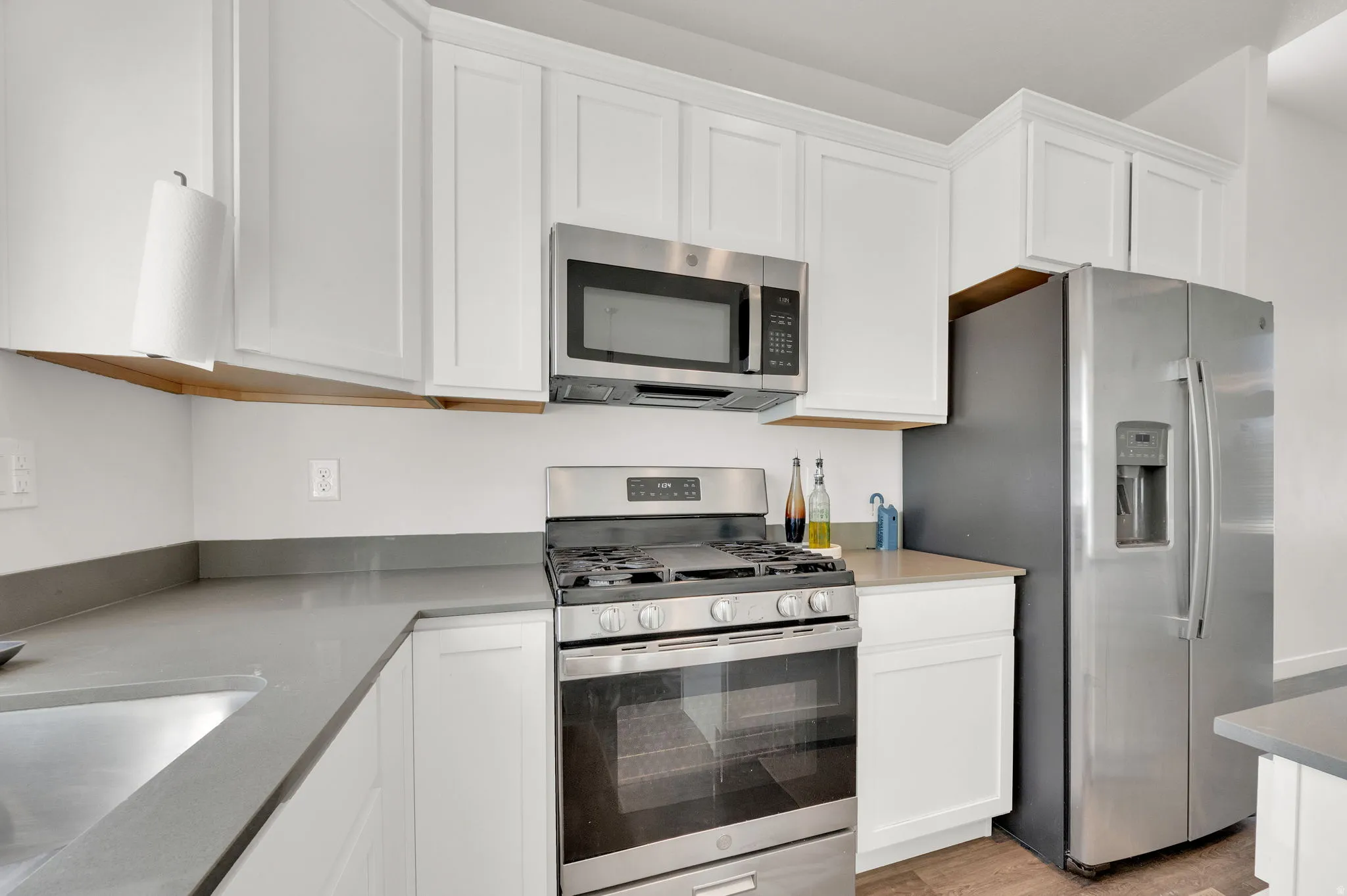 Modern kitchen featuring white shaker cabinetry, stainless steel appliances, gray countertops, a gas range, and wood-finish flooring