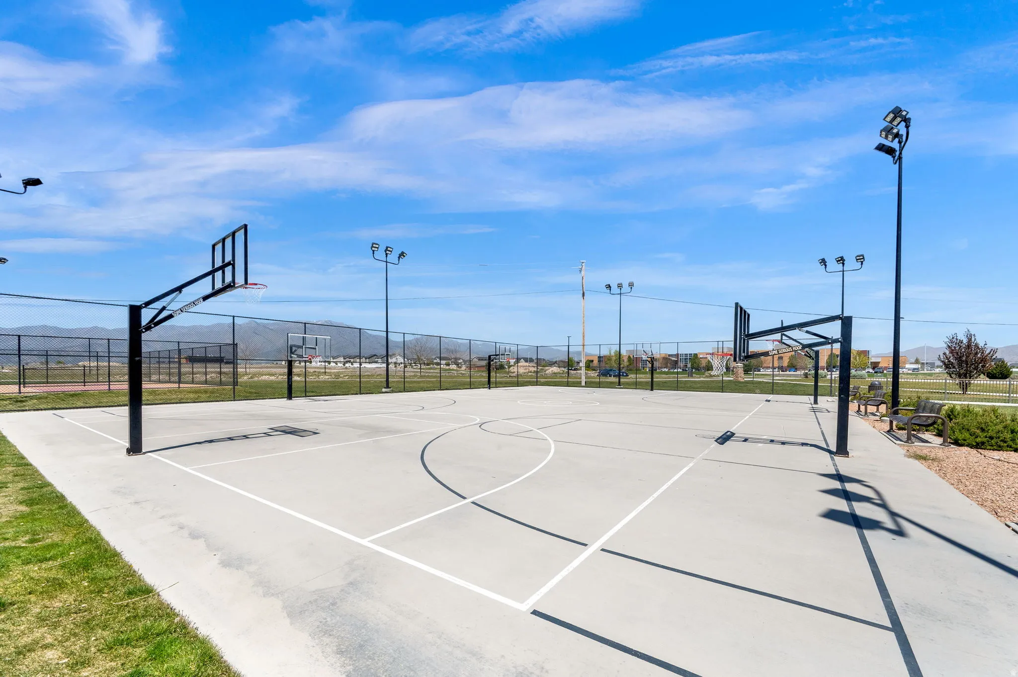 Outdoor basketball court featuring two hoops with backboards, court markings, and perimeter fencing