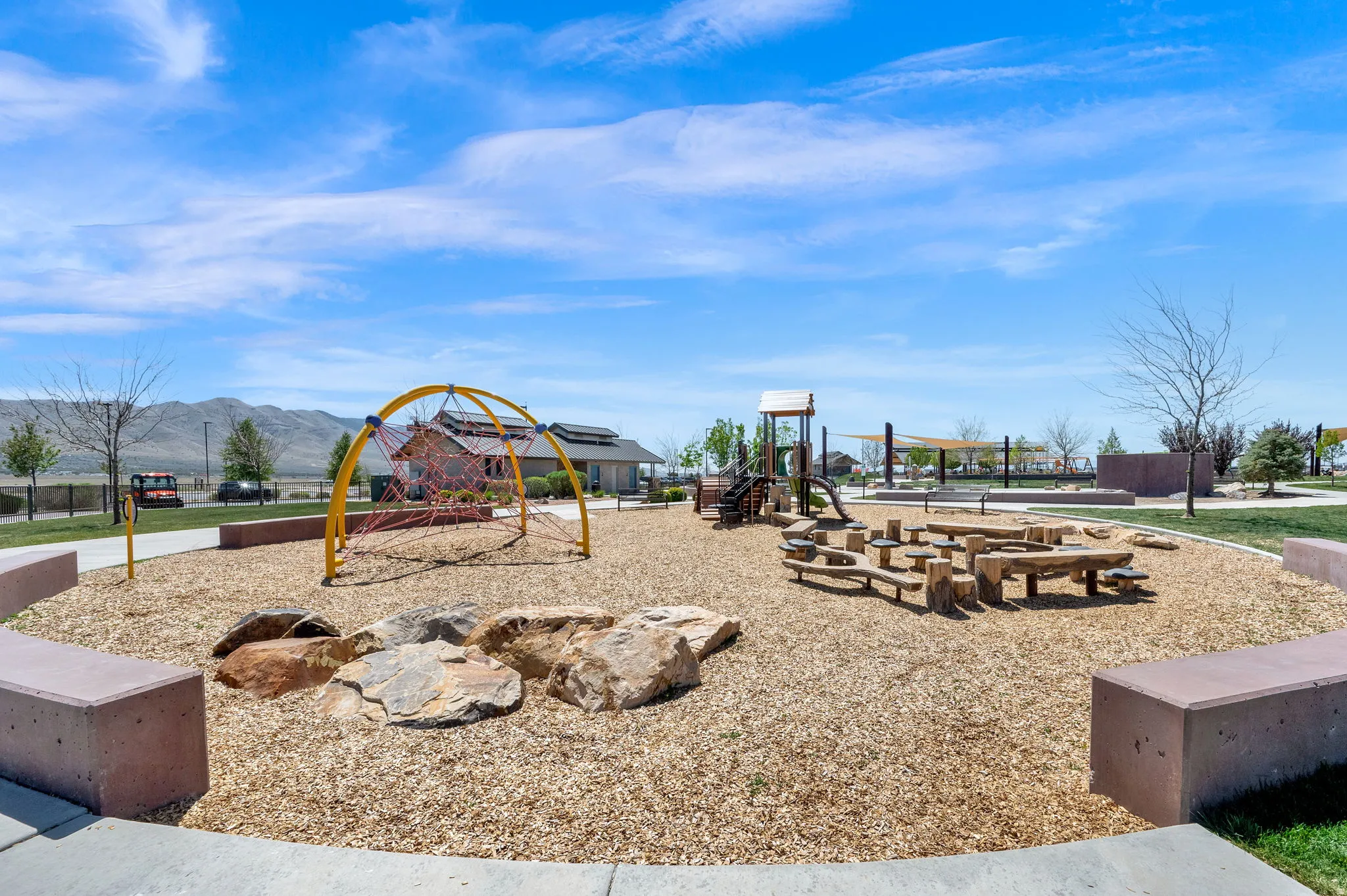 Community park featuring varied play structures, natural rock elements, and concrete seating