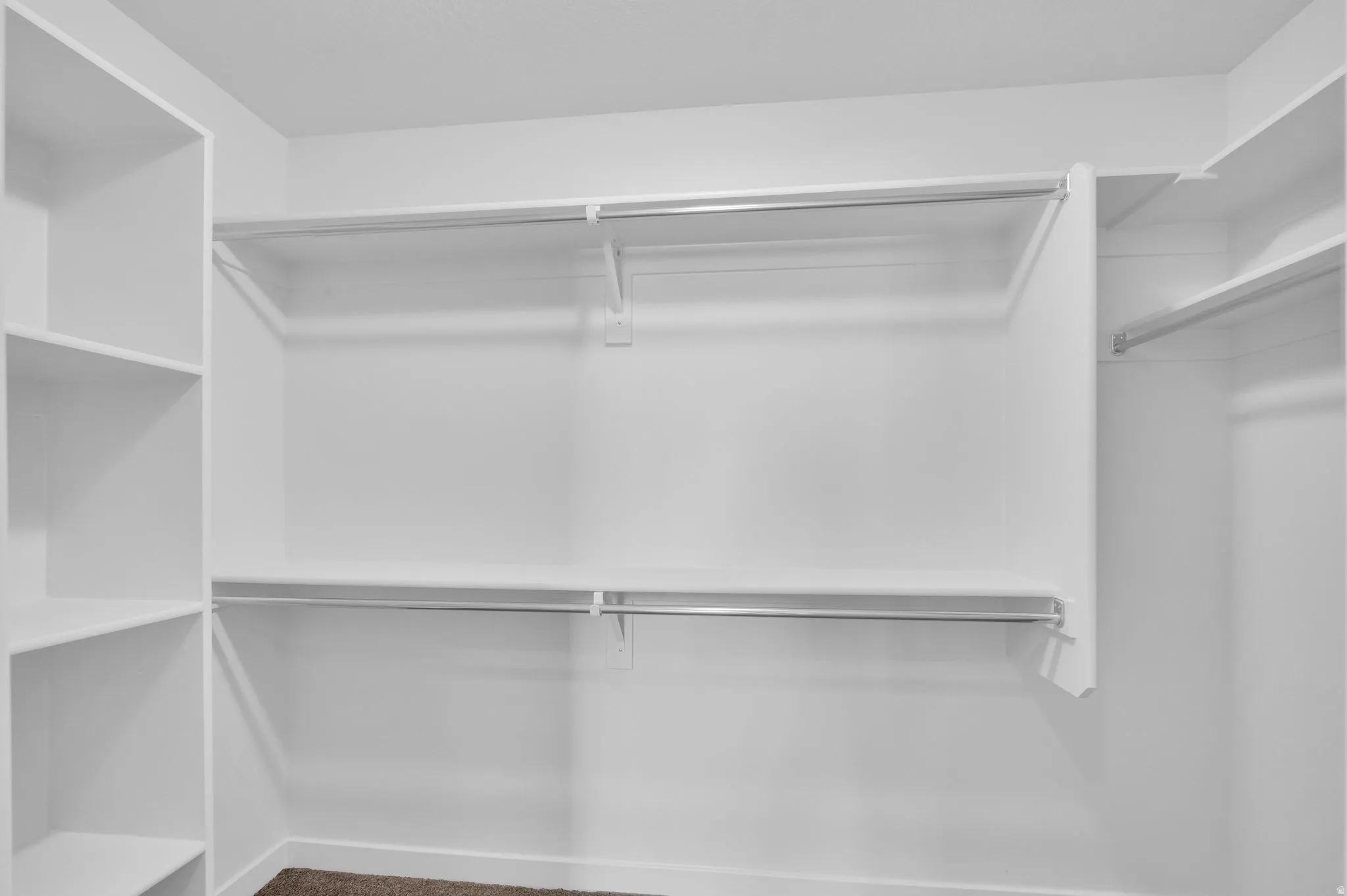 Walk-in closet featuring white built-in shelving, multiple hanging rods, and neutral-toned carpeting