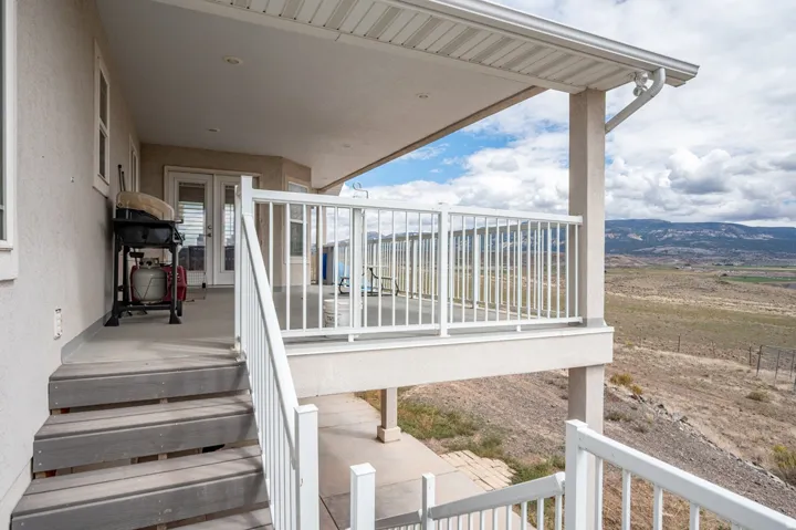 Covered patio featuring a white railing system, direct access via double doors, and an exterior staircase