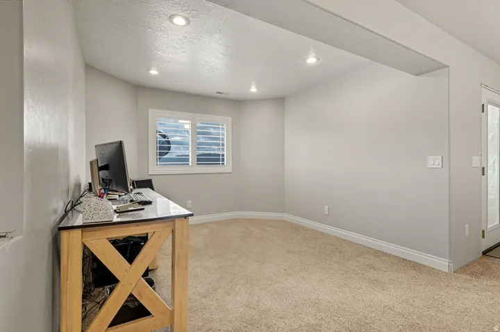 Carpeted room with recessed lighting and a window featuring white plantation shutters