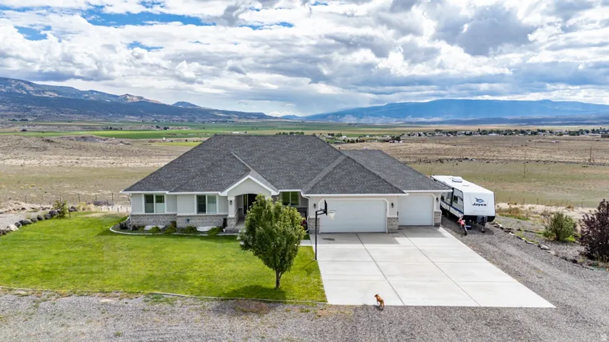 Modern ranch-style residence featuring a gray exterior with stone accents, a dark gray shingle roof, and an attached three-car garage