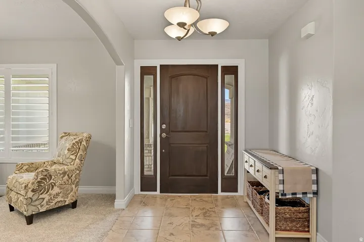 Entryway featuring a dark wood front door with sidelight windows, overhead chandelier lighting, and large format floor tiling