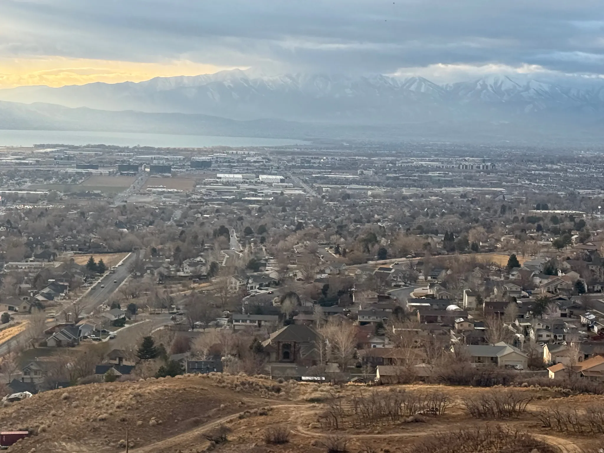 Expansive regional panorama featuring distant snow-capped mountains, a large body of water, and a widespread residential landscape
