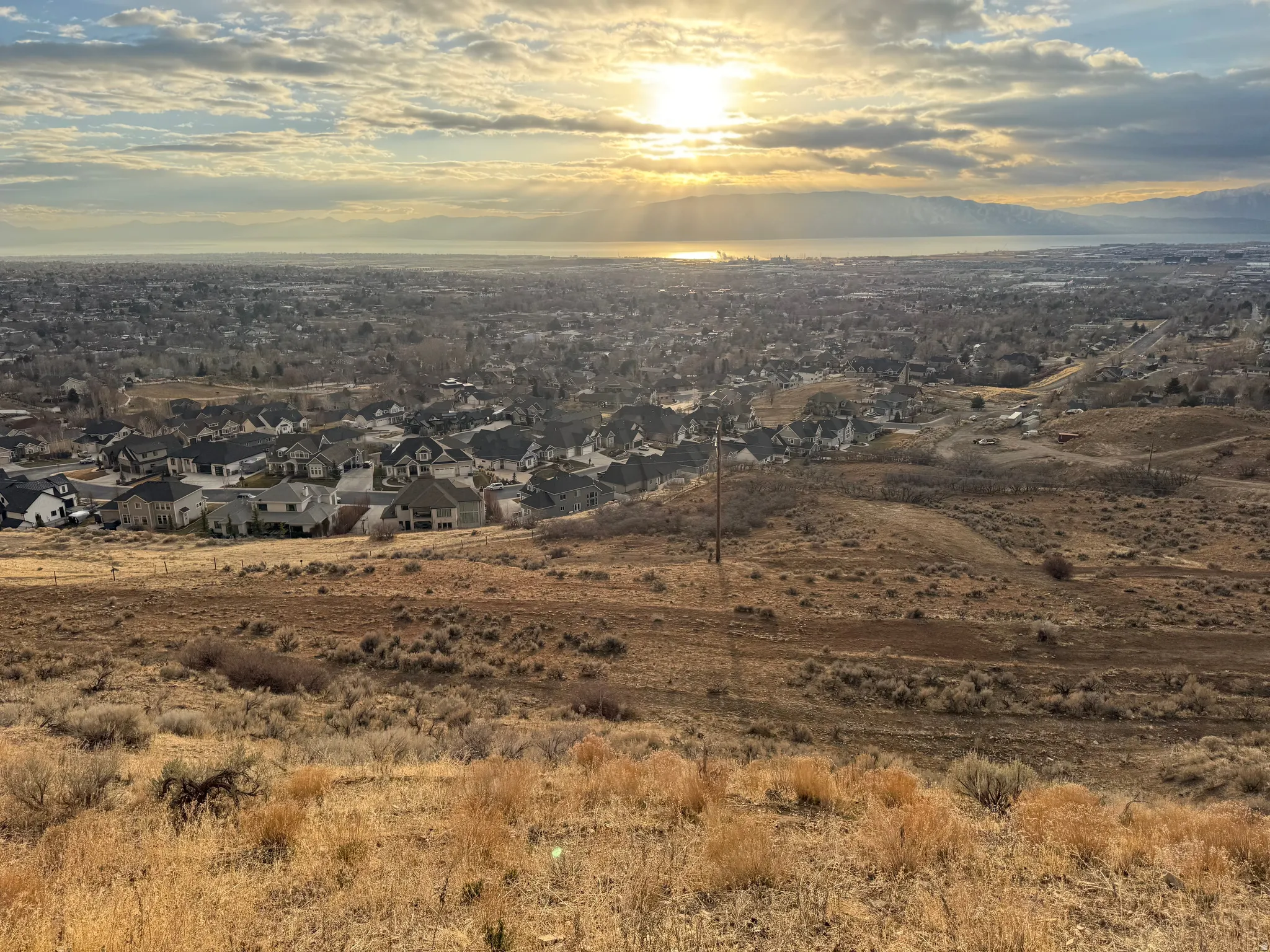 Expansive residential landscape featuring a distant body of water, mountains, and a clear sky with visible sunlight