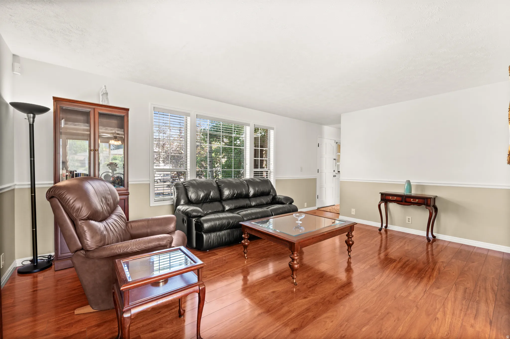 Bright living area featuring wood-finish flooring, white and neutral two-tone wall paint, and multiple windows with blinds