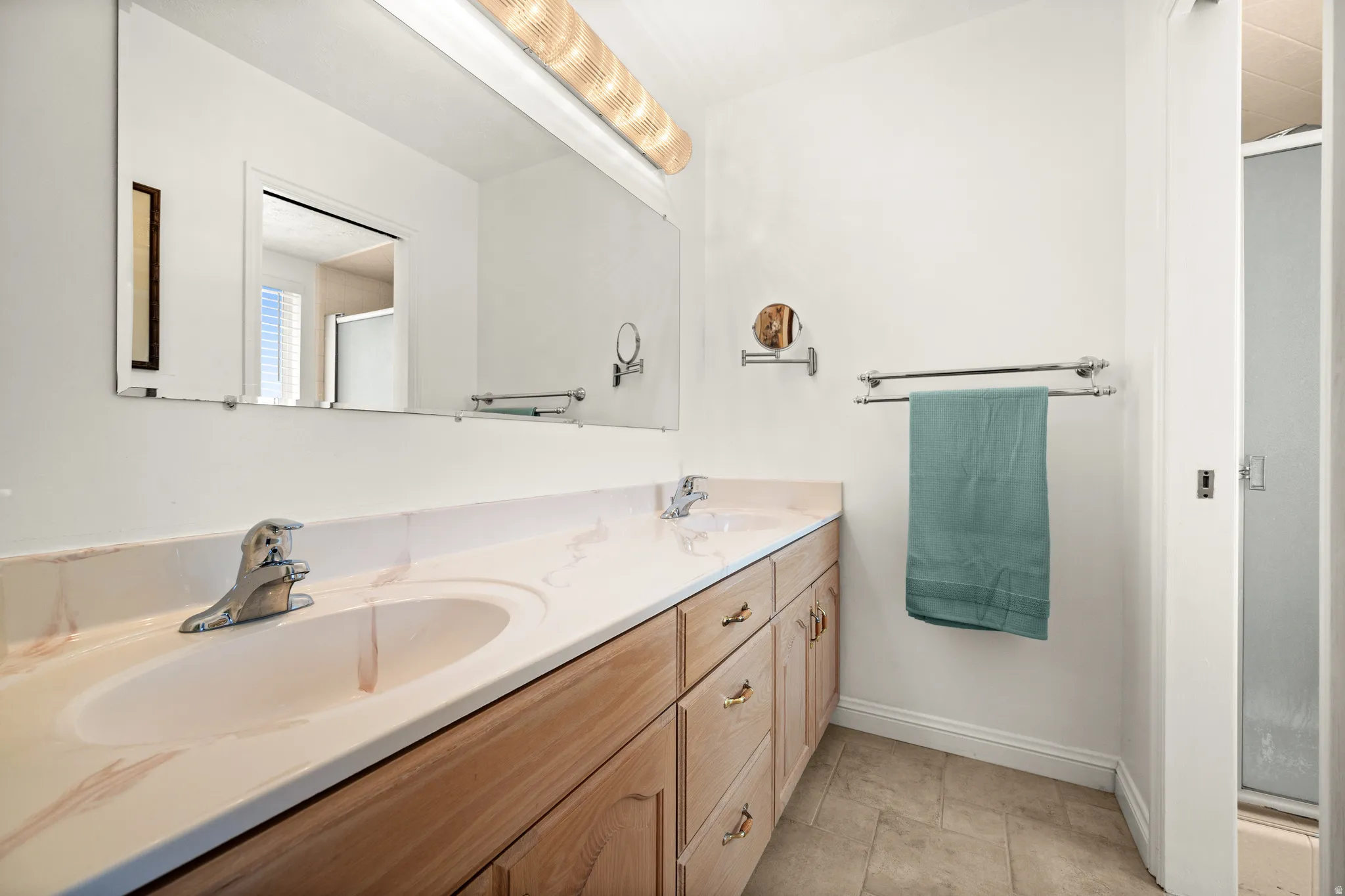 Double vanity with integrated sinks, light wood-finish cabinetry, and a large wall-mounted mirror